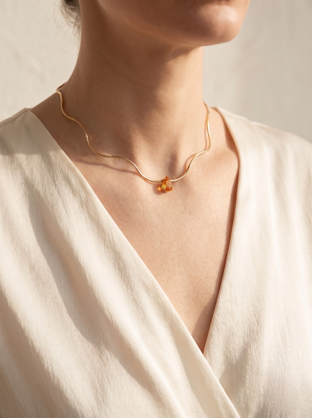 Woman wearing StoneCraft Jewellery Gold Wave Snake Chain Necklace with orange Crystal Pendant full neckline view on cream wrap top