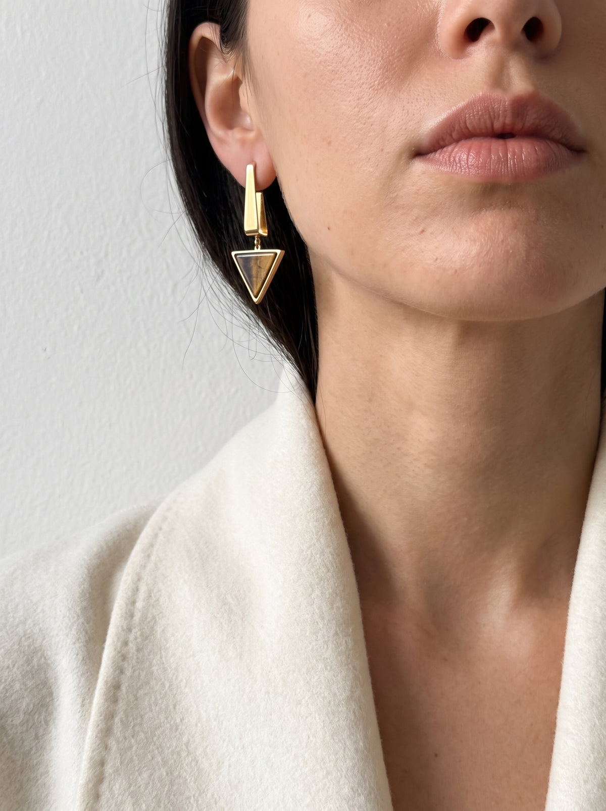 Model wearing StoneCraft Jewellery gold-plated Tiger’s Eye triangle drop earrings with a cream jacket.