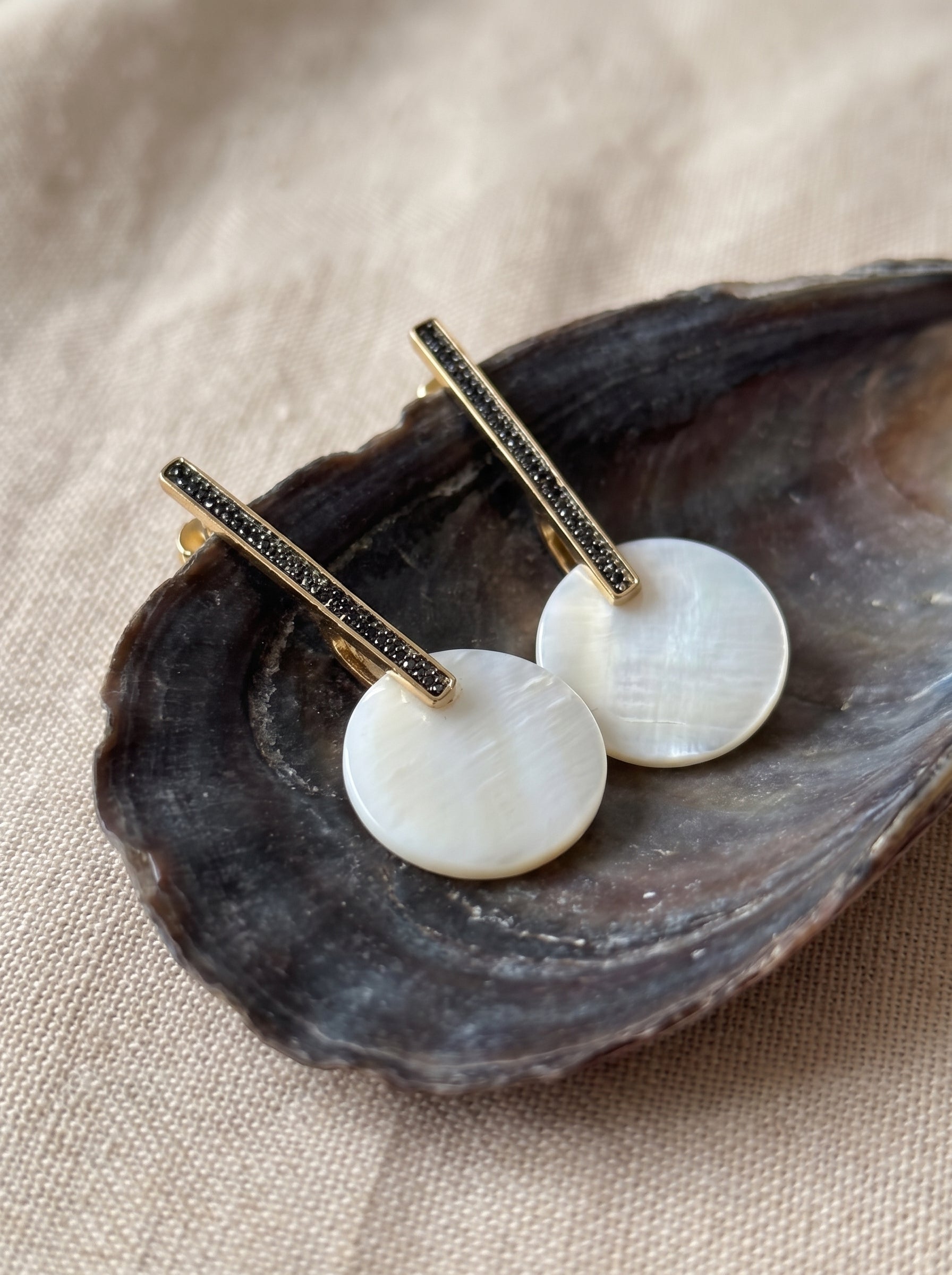 Pair of mother of pearl bar drop earrings resting inside an oyster shell
