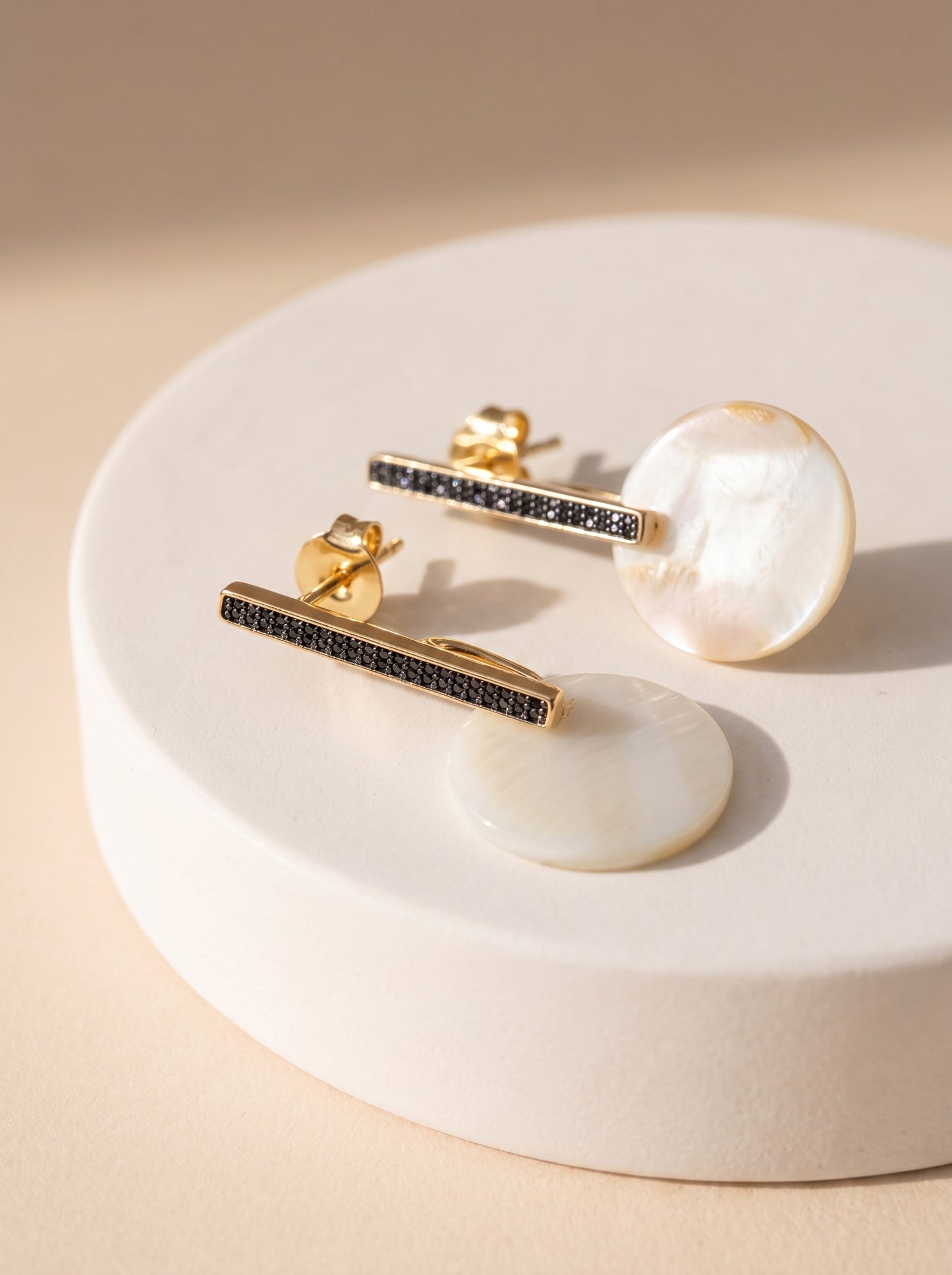 Two mother of pearl bar drop earrings displayed on a white ceramic stand, showing front and back