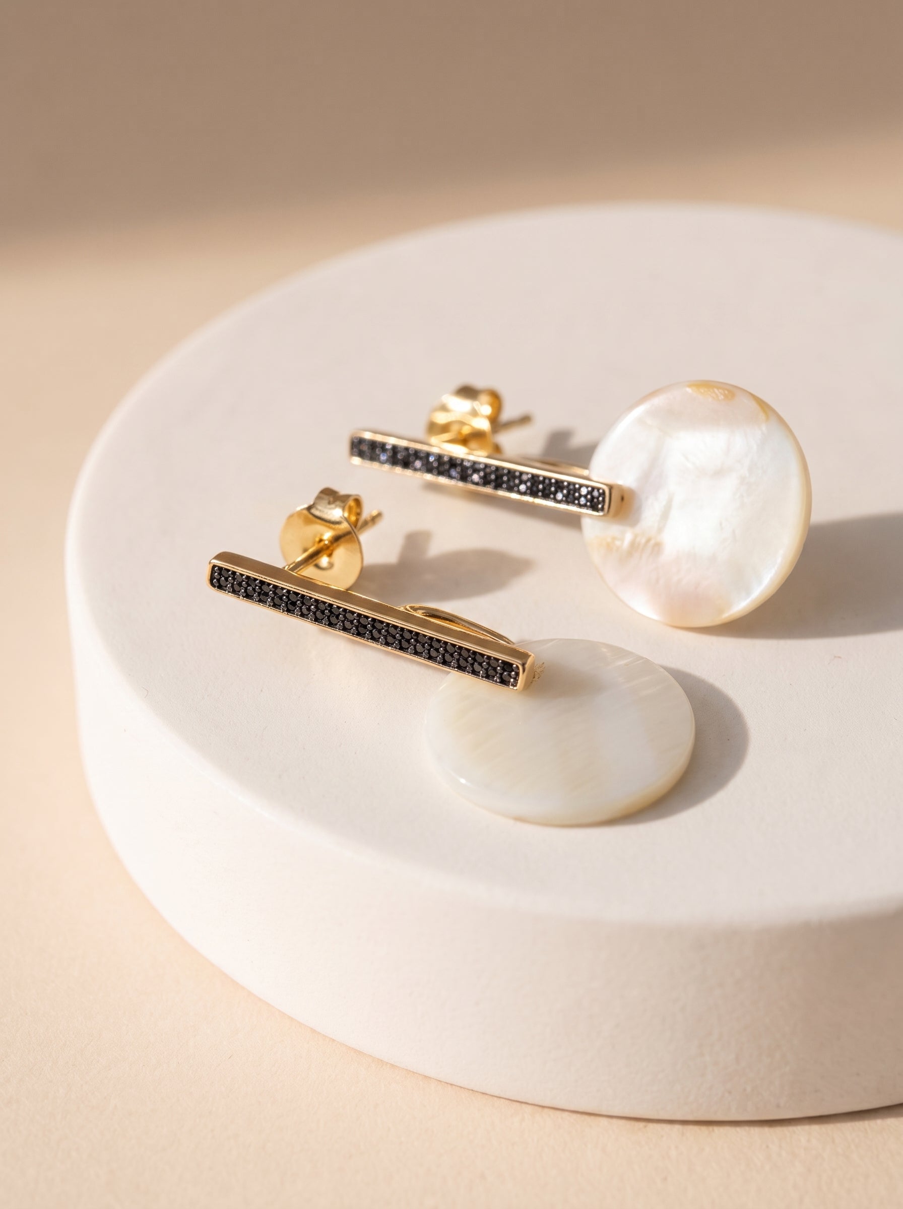 Two mother of pearl bar drop earrings displayed on a white ceramic stand, showing front and back