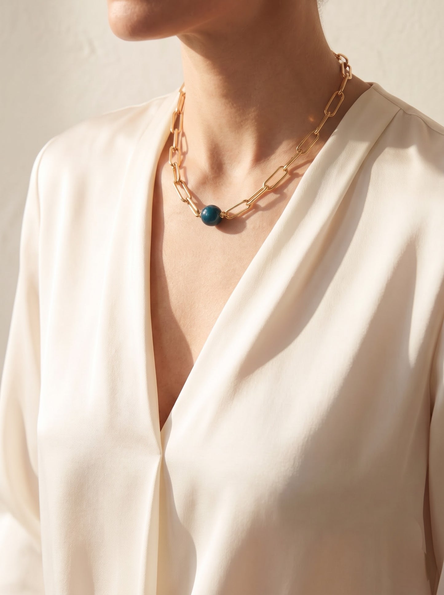 Woman wearing StoneCraft Jewellery apatite gemstone sphere gold paperclip chain necklace, draped cream wrap top styling.
