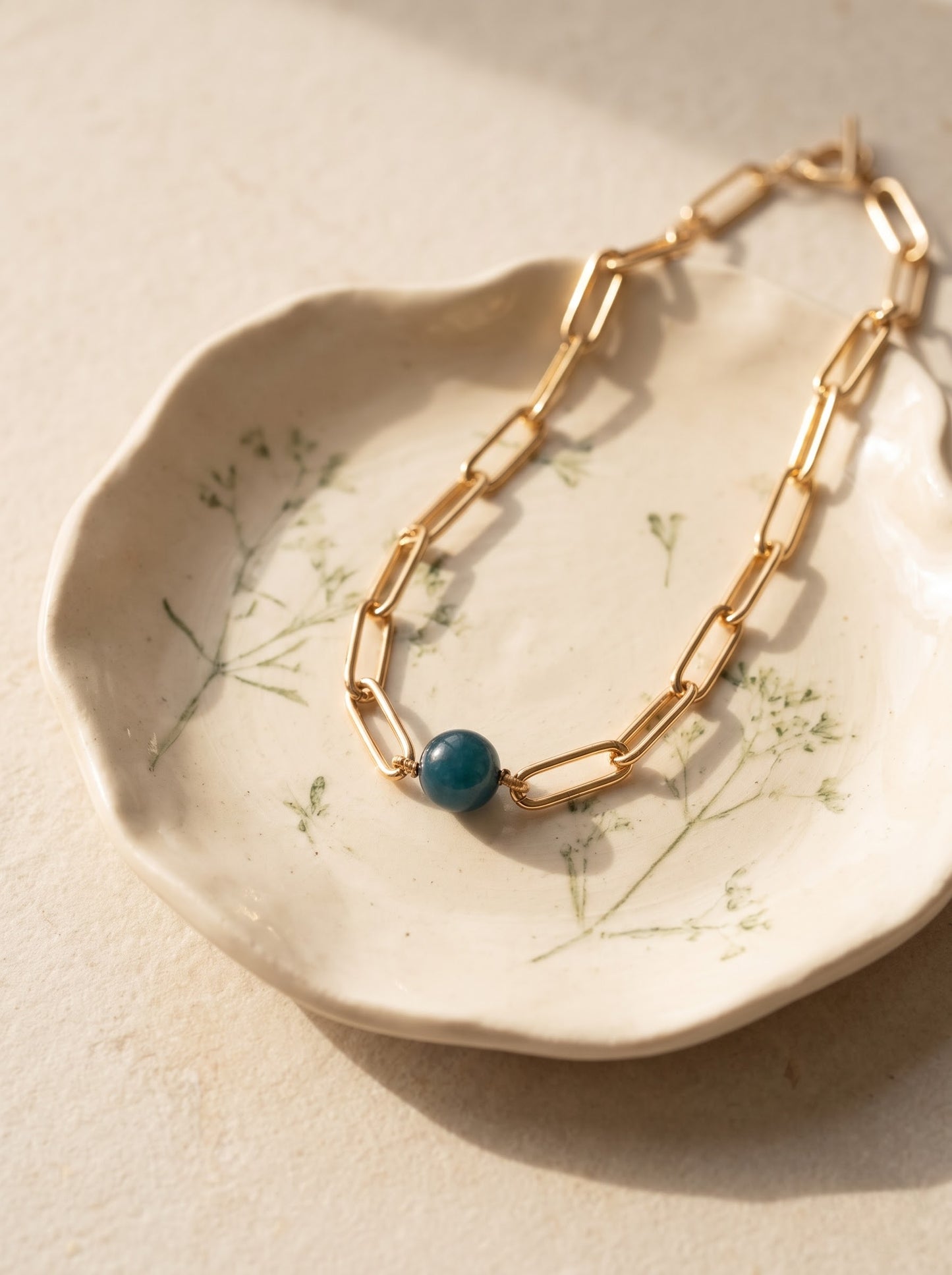 StoneCraft Jewellery apatite gemstone sphere gold paperclip chain necklace, flat lay on floral ceramic dish.