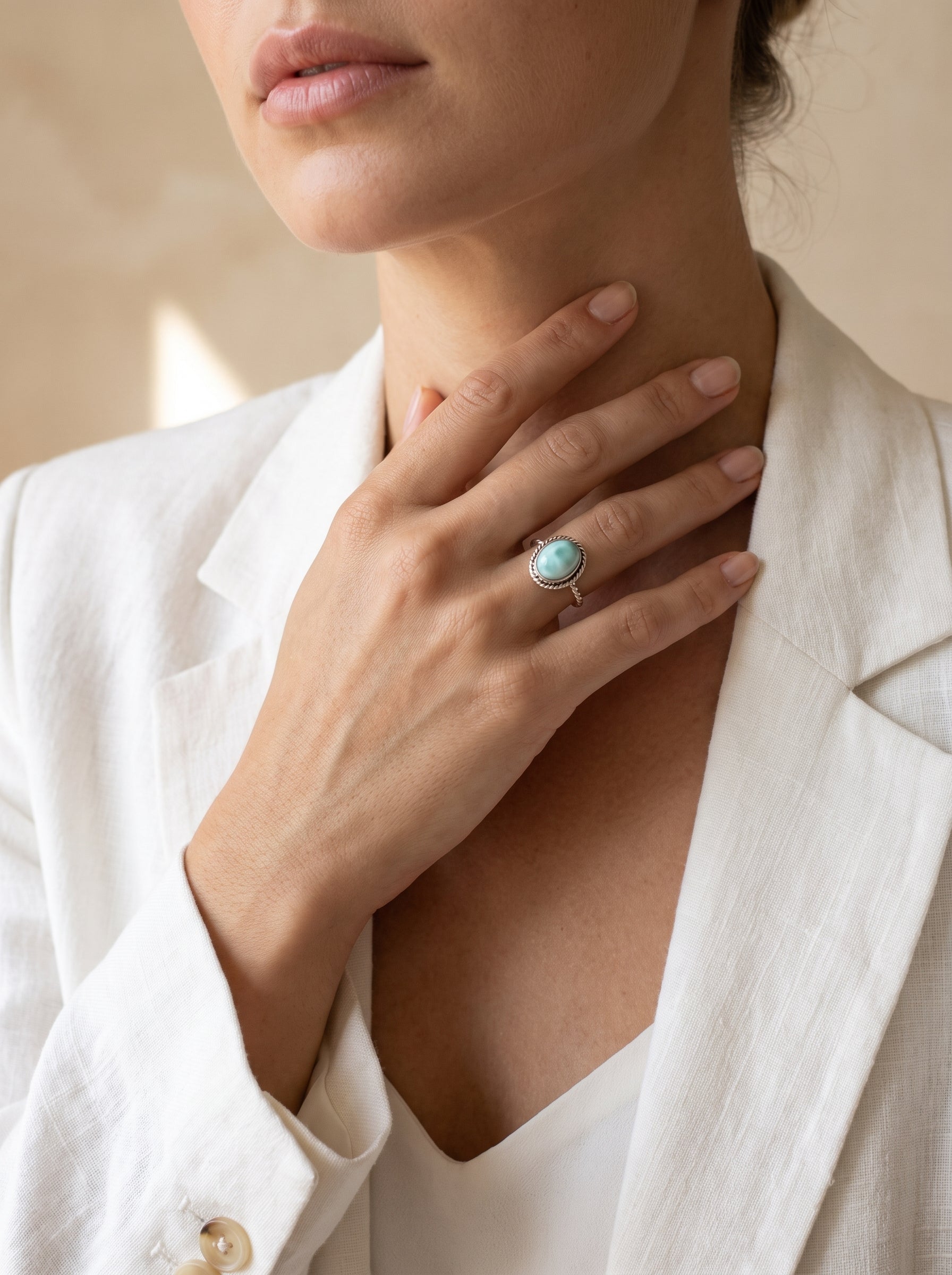 A close-up lifestyle shot of a model wearing a silver ring with a round larimar cabochon on her finger, styled with a white linen blazer.