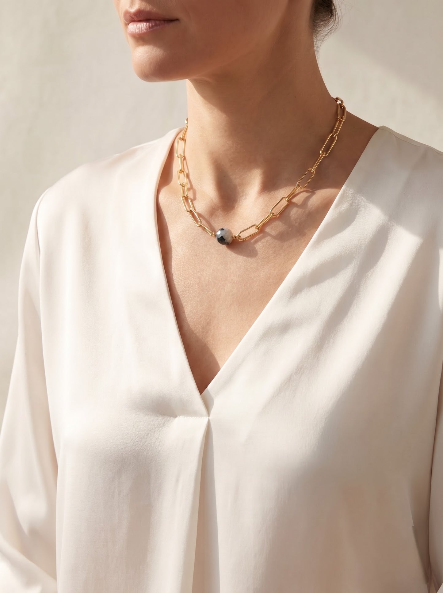 Woman wearing StoneCraft Jewellery black rutile quartz sphere gold paperclip chain necklace, V-neck white silk blouse styling.