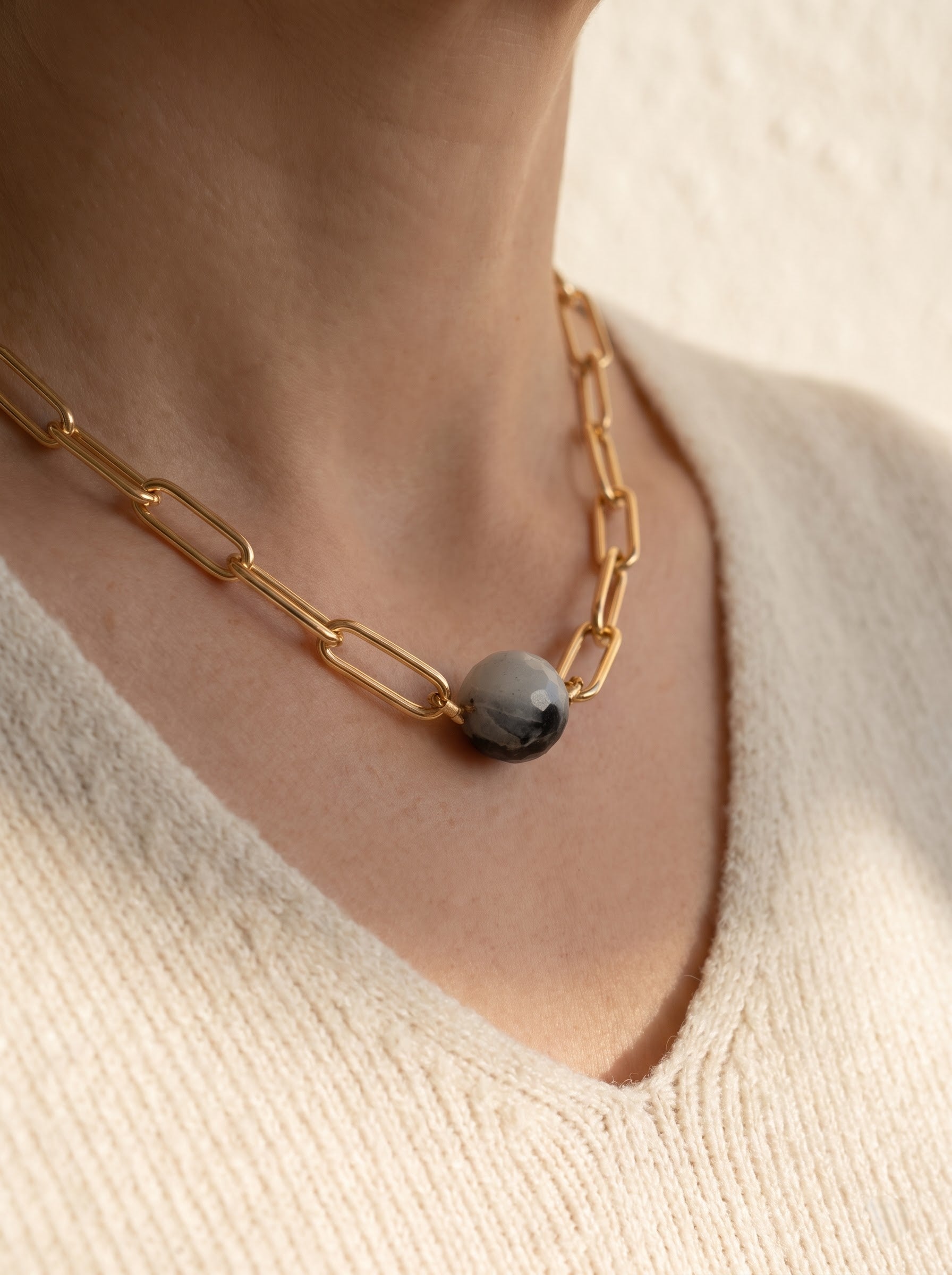 Woman wearing StoneCraft Jewellery black rutile quartz sphere gold paperclip chain necklace, cream knit top close-up decolletage.