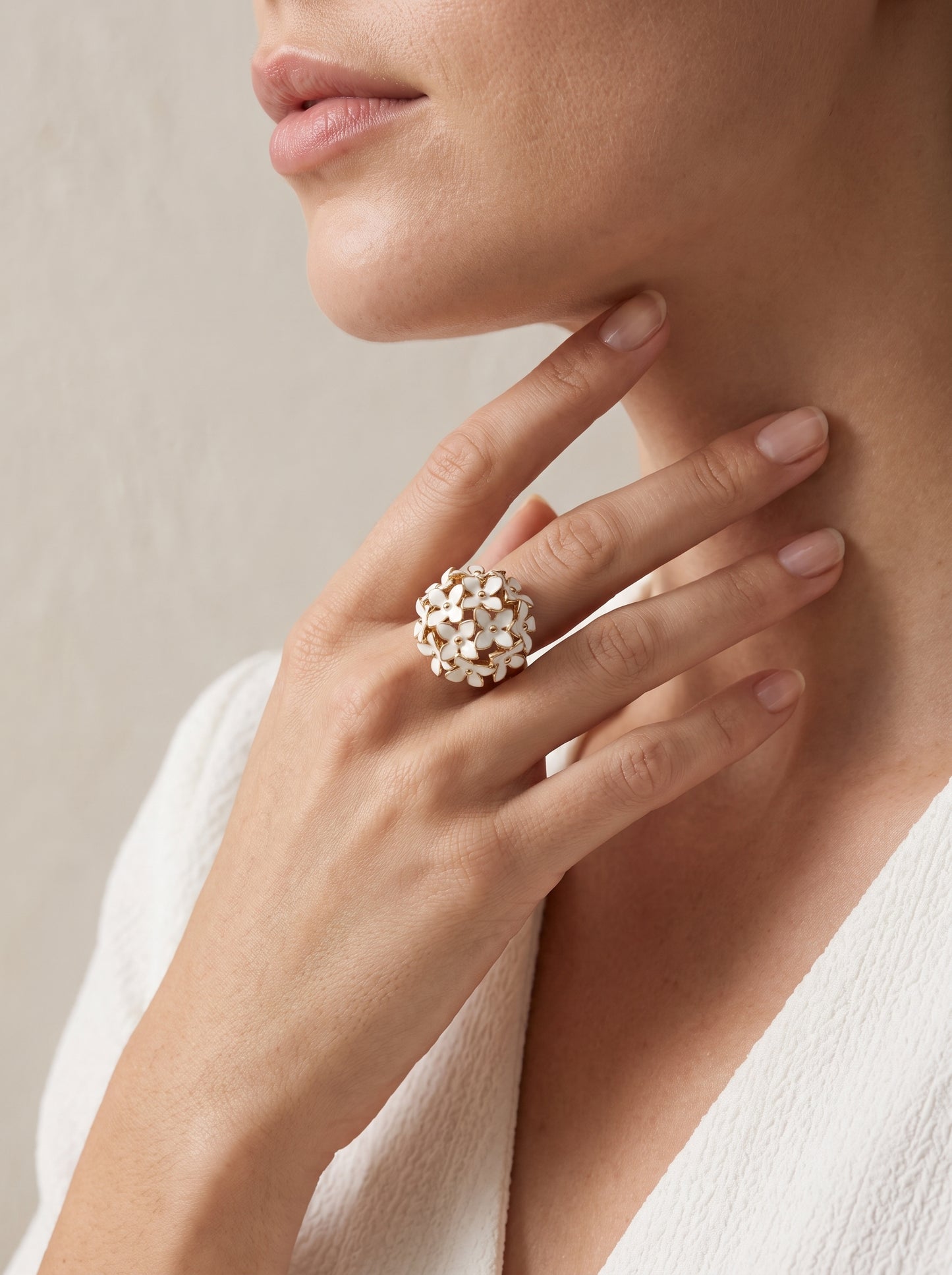 A close-up lifestyle shot of a model wearing a large, textured gold ring with small white floral or leaf-like details on one finger.