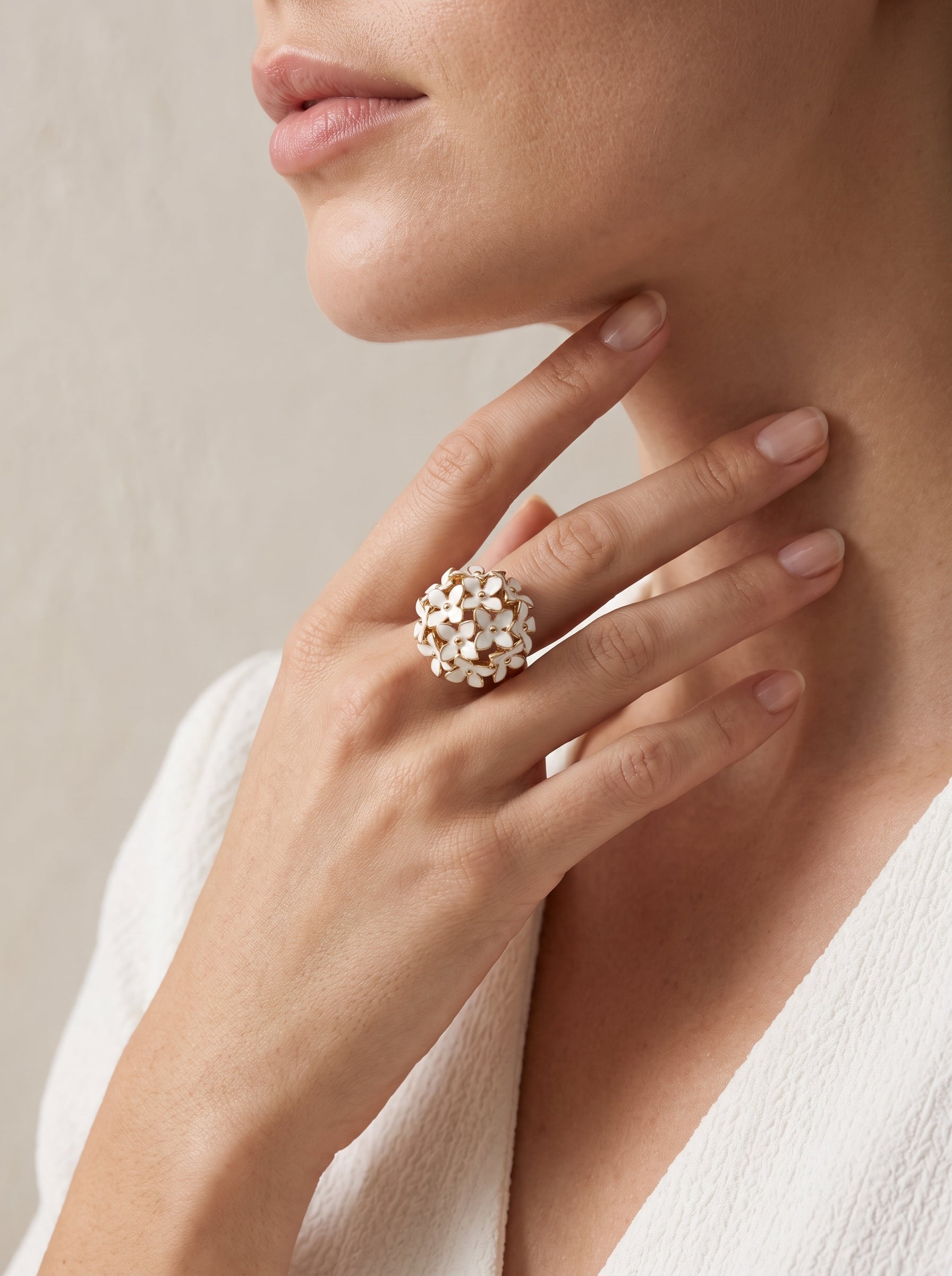 A close-up lifestyle shot of a model wearing a large, textured gold ring with small white floral or leaf-like details on one finger.