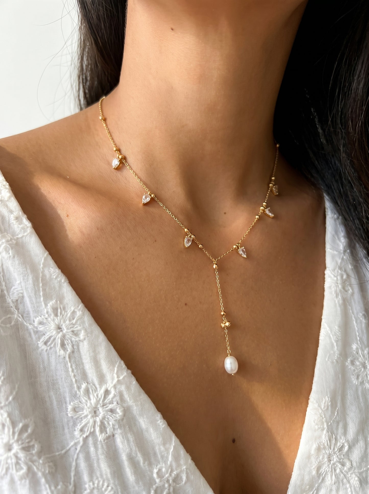 Crystal and pearl lariat necklace worn at neckline, gold-plated delicate chain with crystal accents