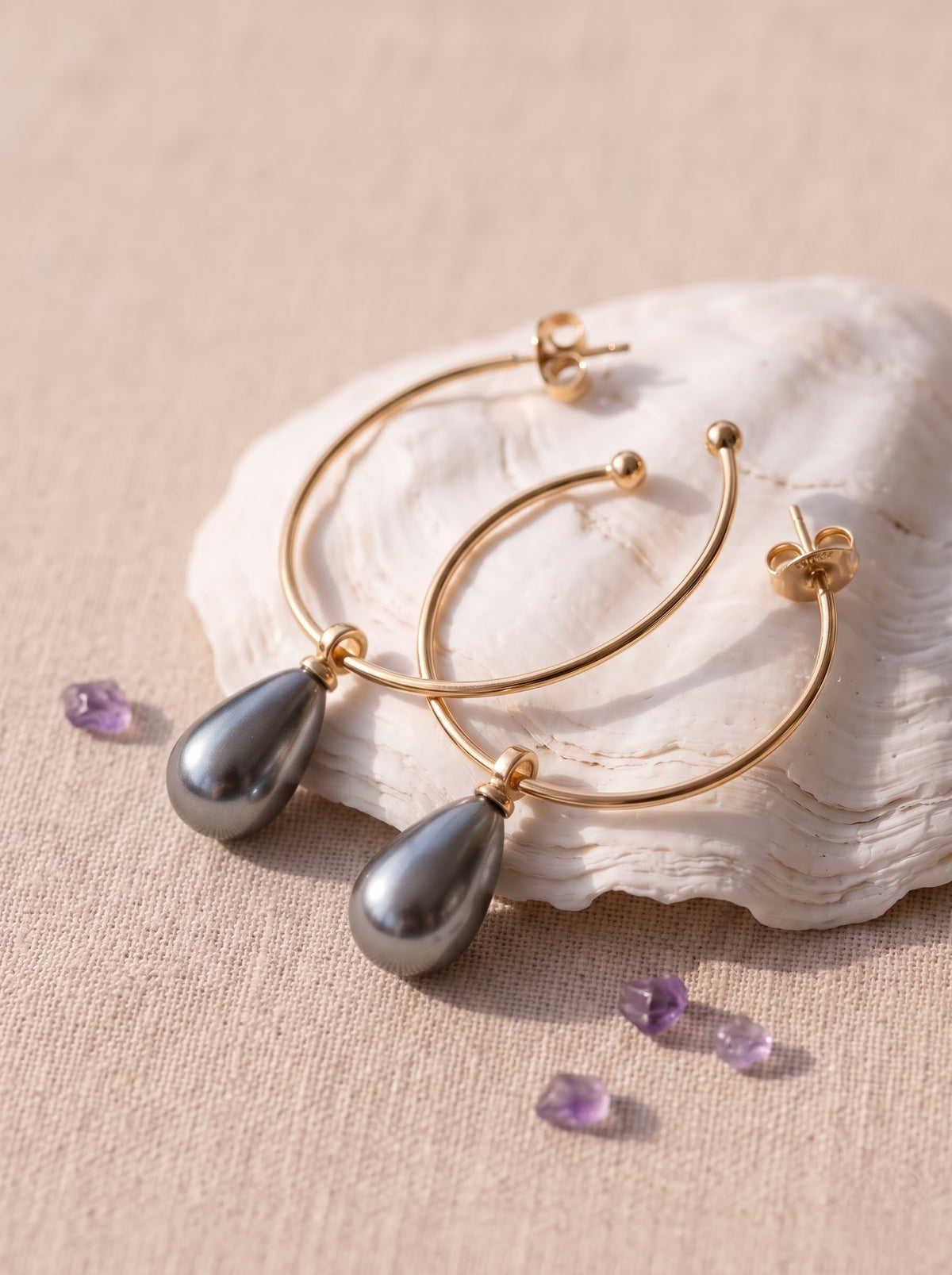 StoneCraft Jewellery gold-plated open hoop earrings with grey pearl teardrop drops resting on a white shell.