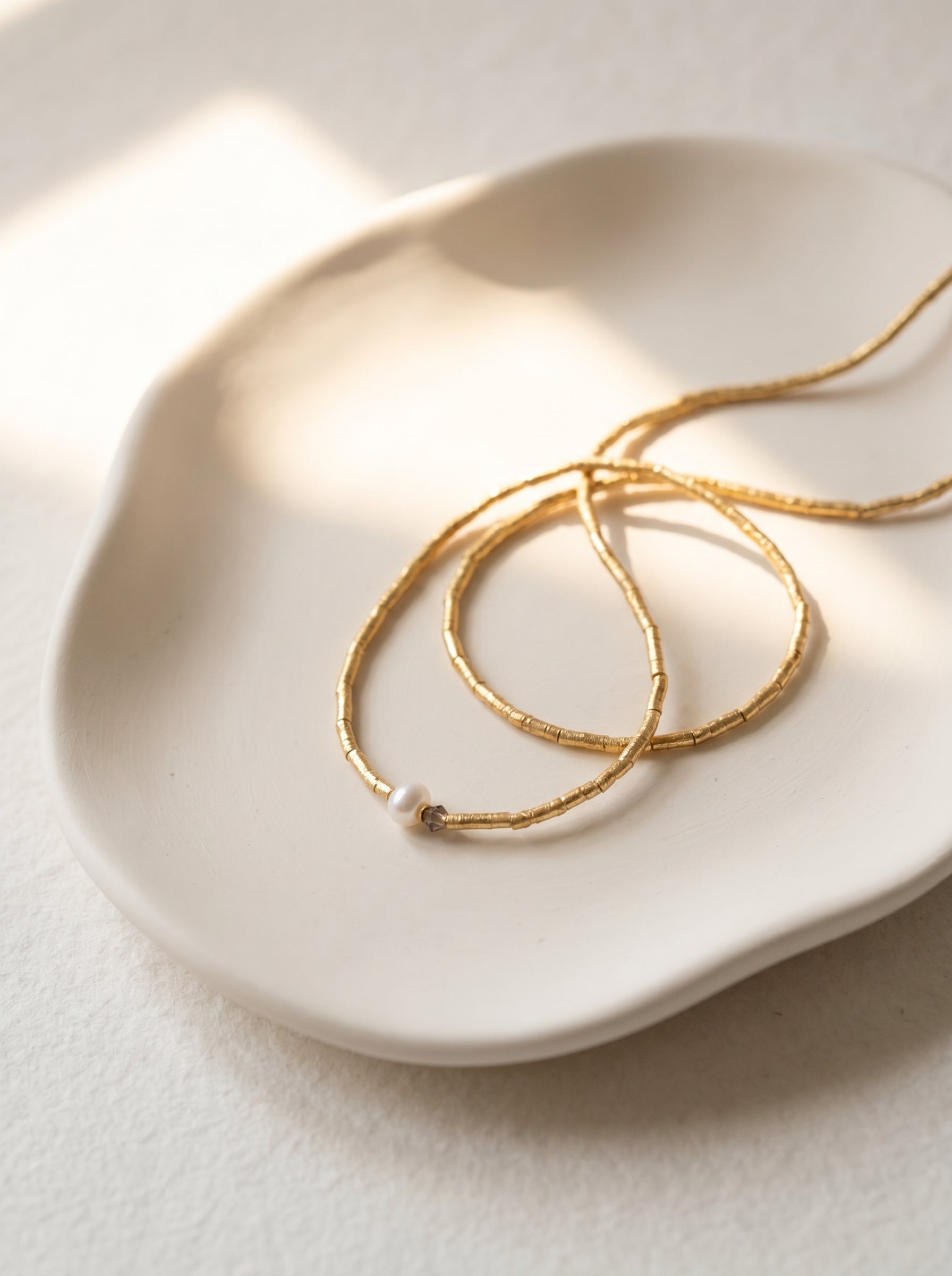 Close-up of white freshwater pearl and crystal pendant on gold-plated beaded necklace