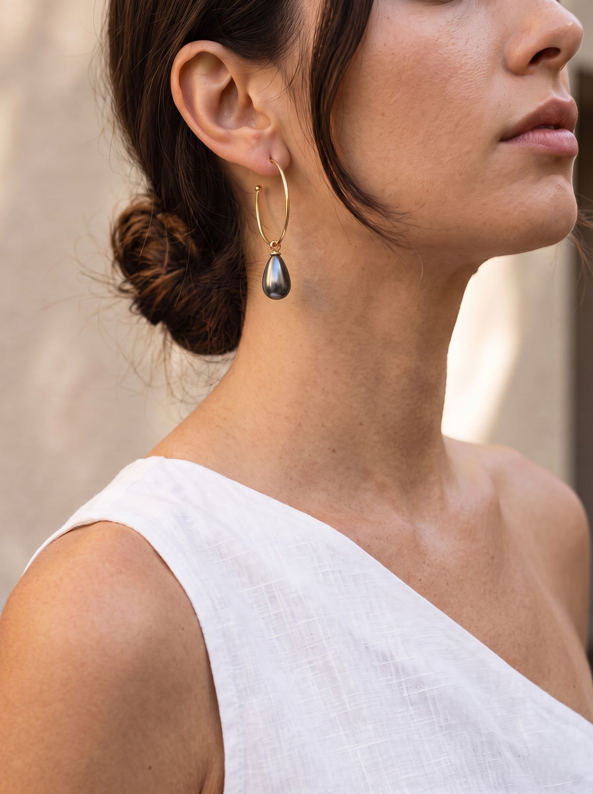 Side-profile model: “Woman in side profile wearing a StoneCraft Jewellery gold-plated open hoop earring with a grey pearl drop.