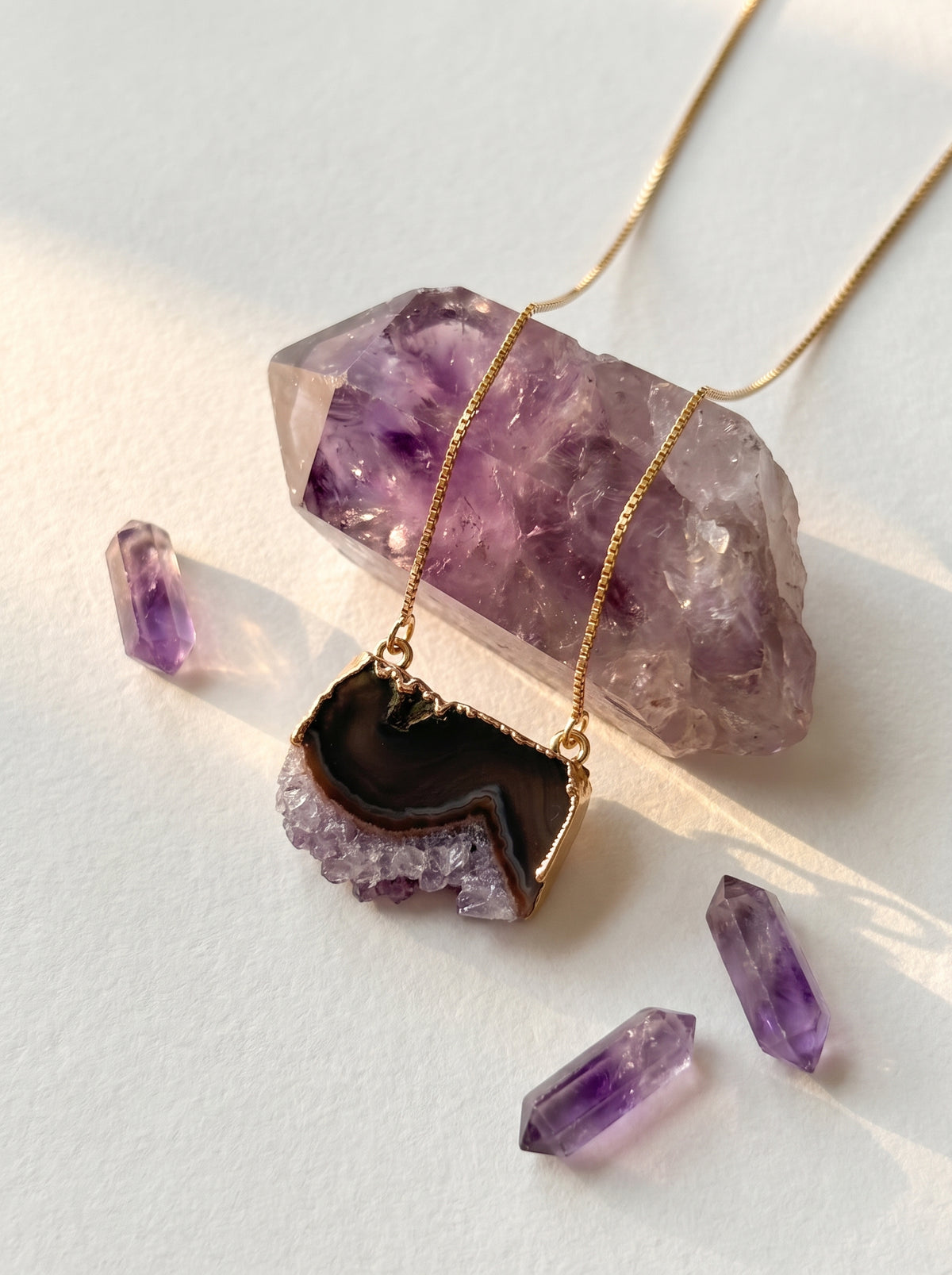 StoneCraft Jewellery purple crystal slice pendant necklace on a white surface beside purple crystals.