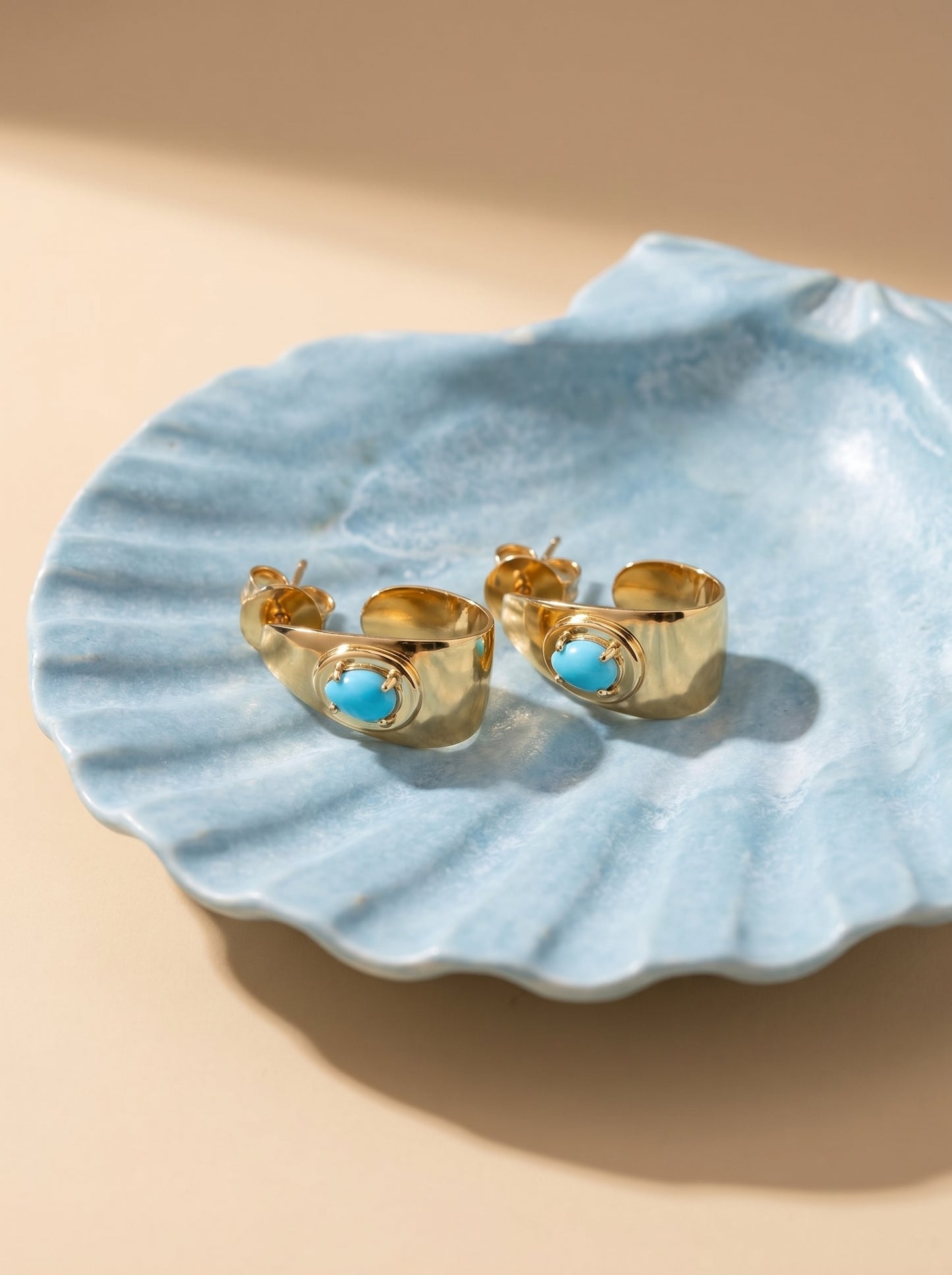 Gold cuff bracelets with turquoise stones on a light blue shell against a beige background