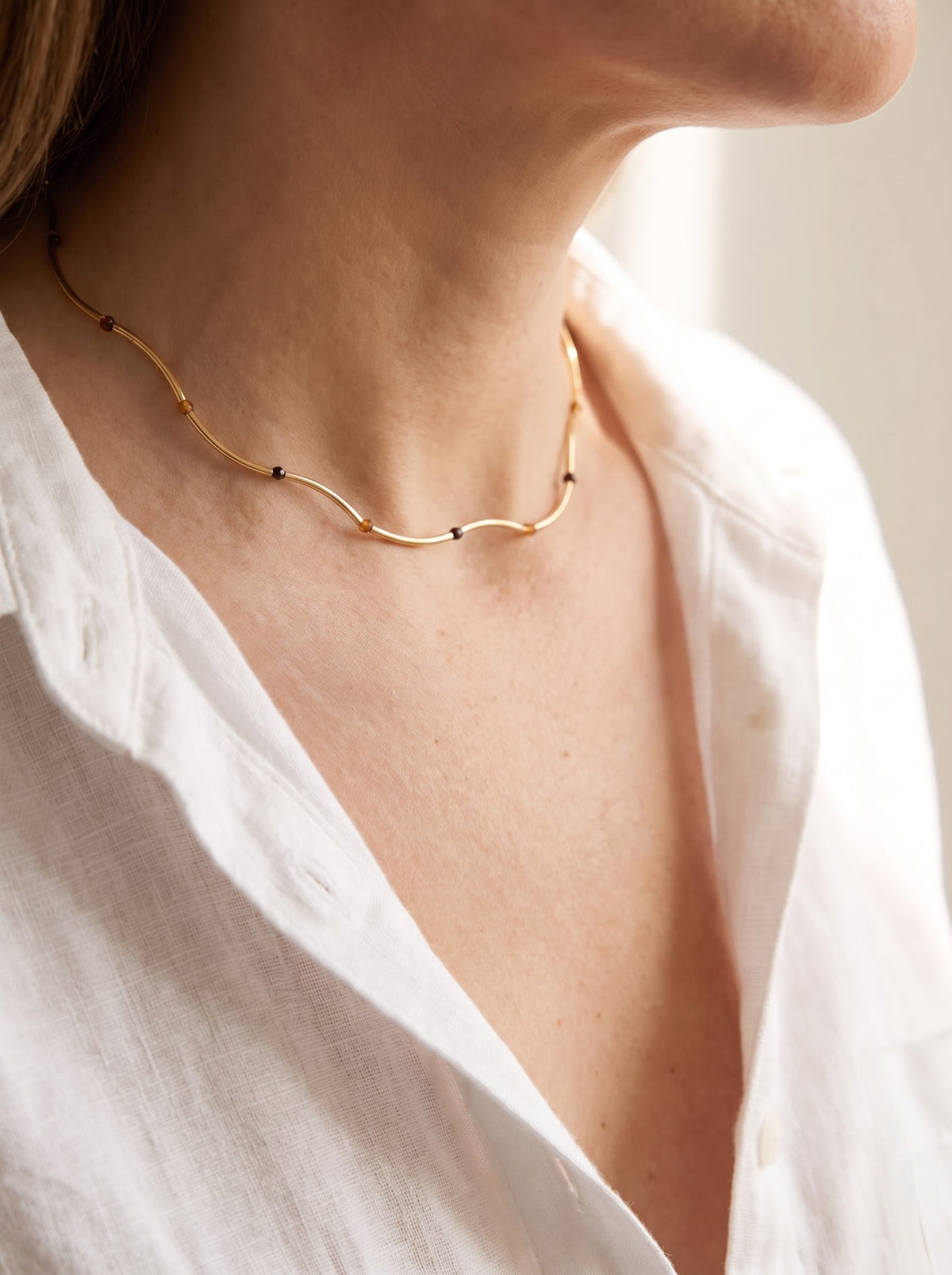 Woman wearing StoneCraft Jewellery Gold Wave Chain Necklace with Tiger's Eye Beads close-up on neck with white linen shirt