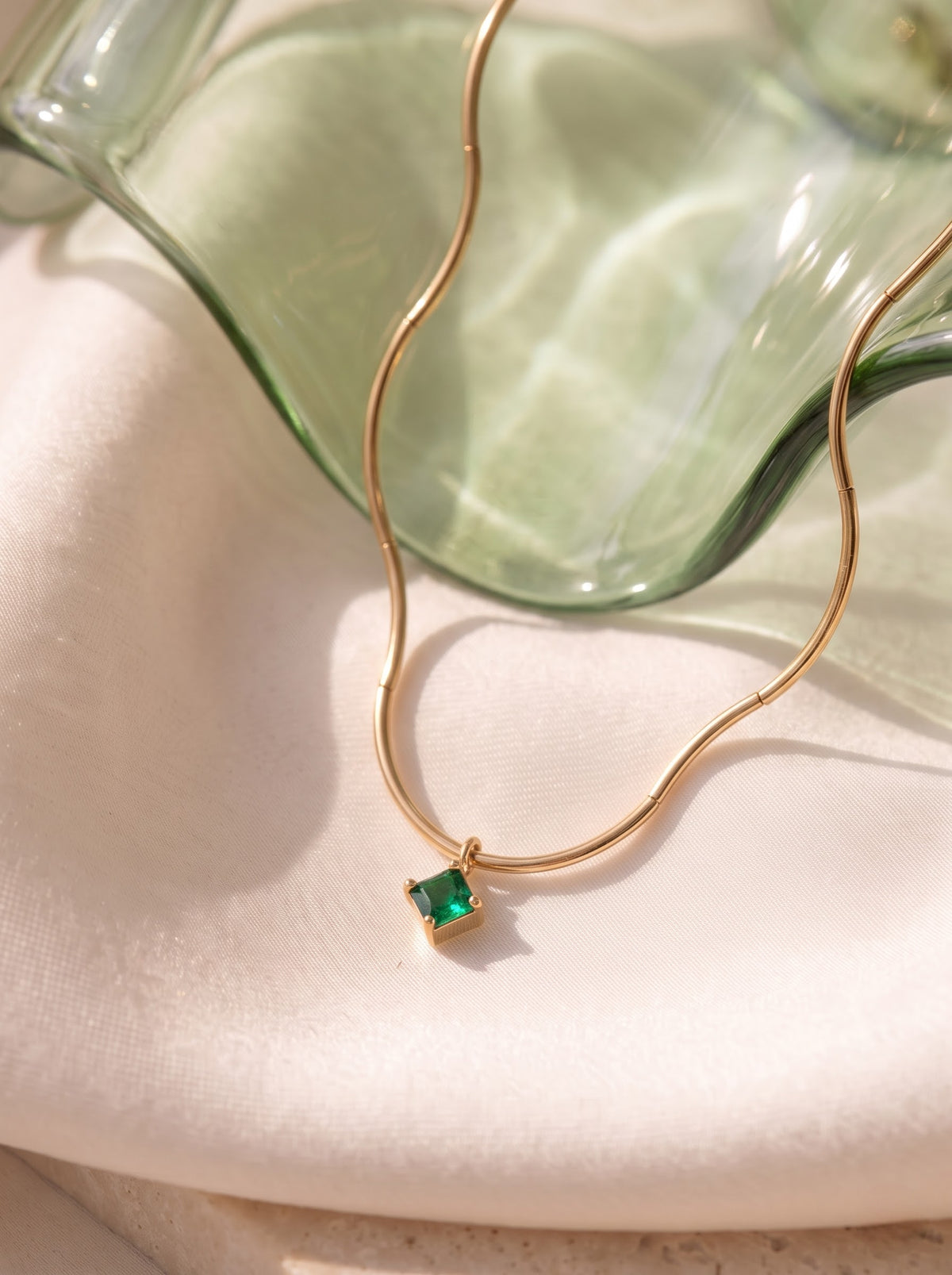 Woman wearing a StoneCraft Jewellery gold wave chain necklace with a square green crystal pendant and a white neckline.
