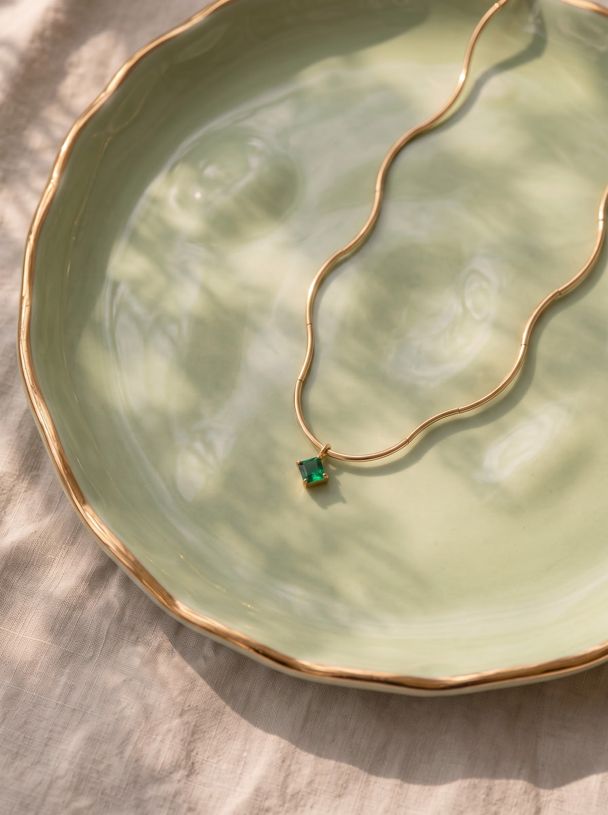StoneCraft Jewellery gold wave chain necklace with a green crystal pendant draped over a curved white display.