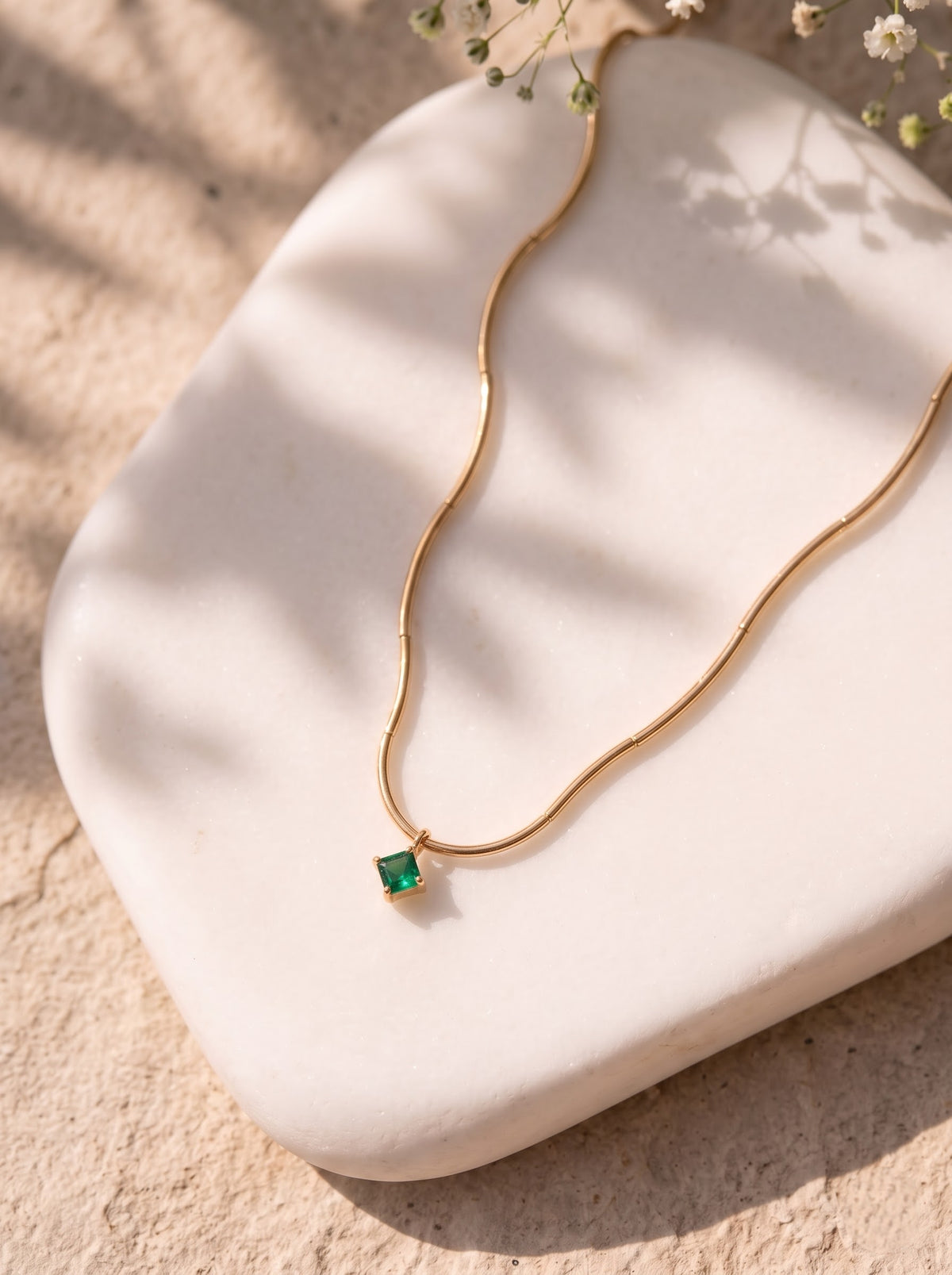 StoneCraft Jewellery gold wave chain necklace with a square green crystal pendant displayed on an upright white stand.