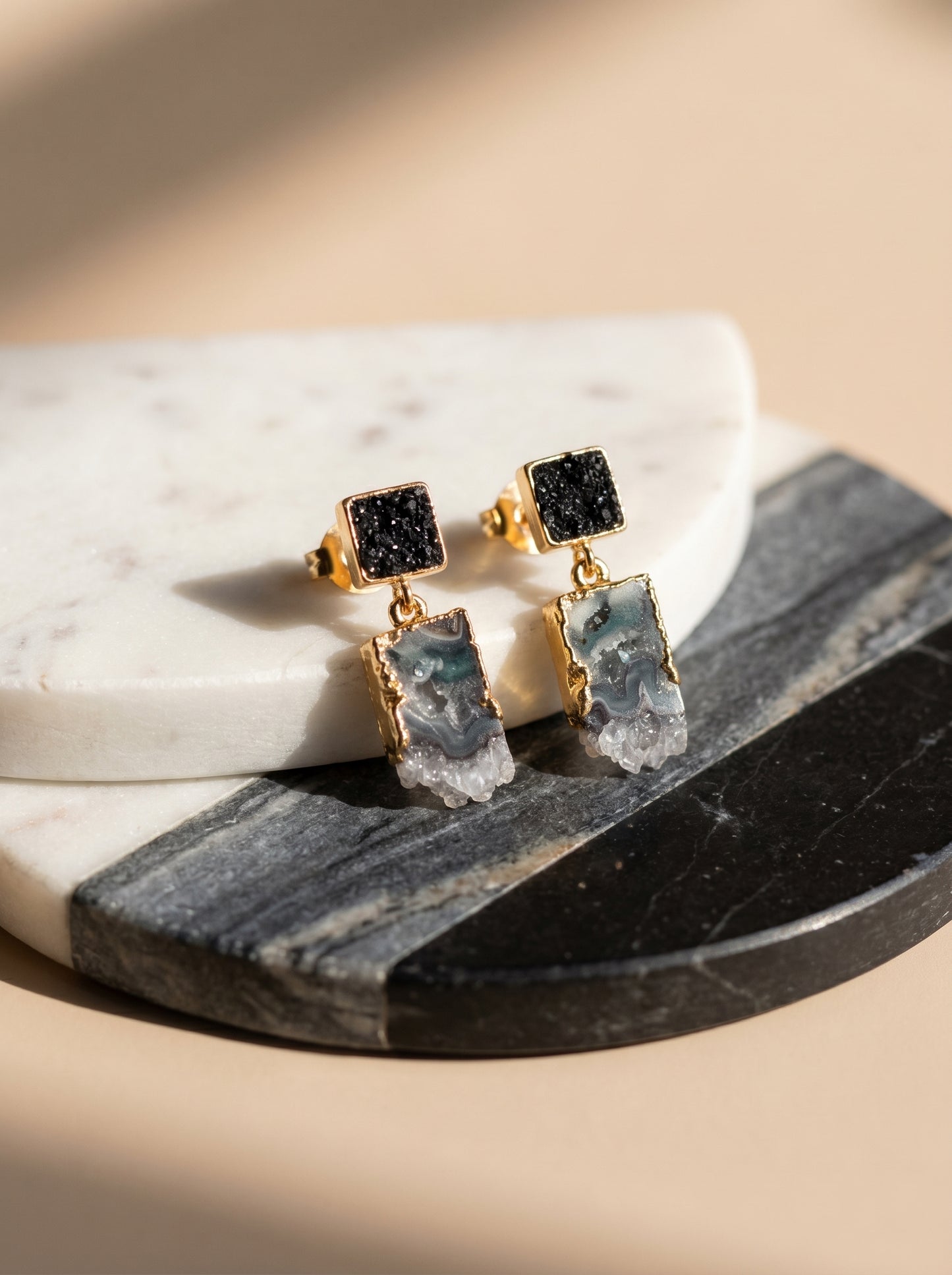 Black tourmaline and amethyst drop earrings flat lay on marble surface