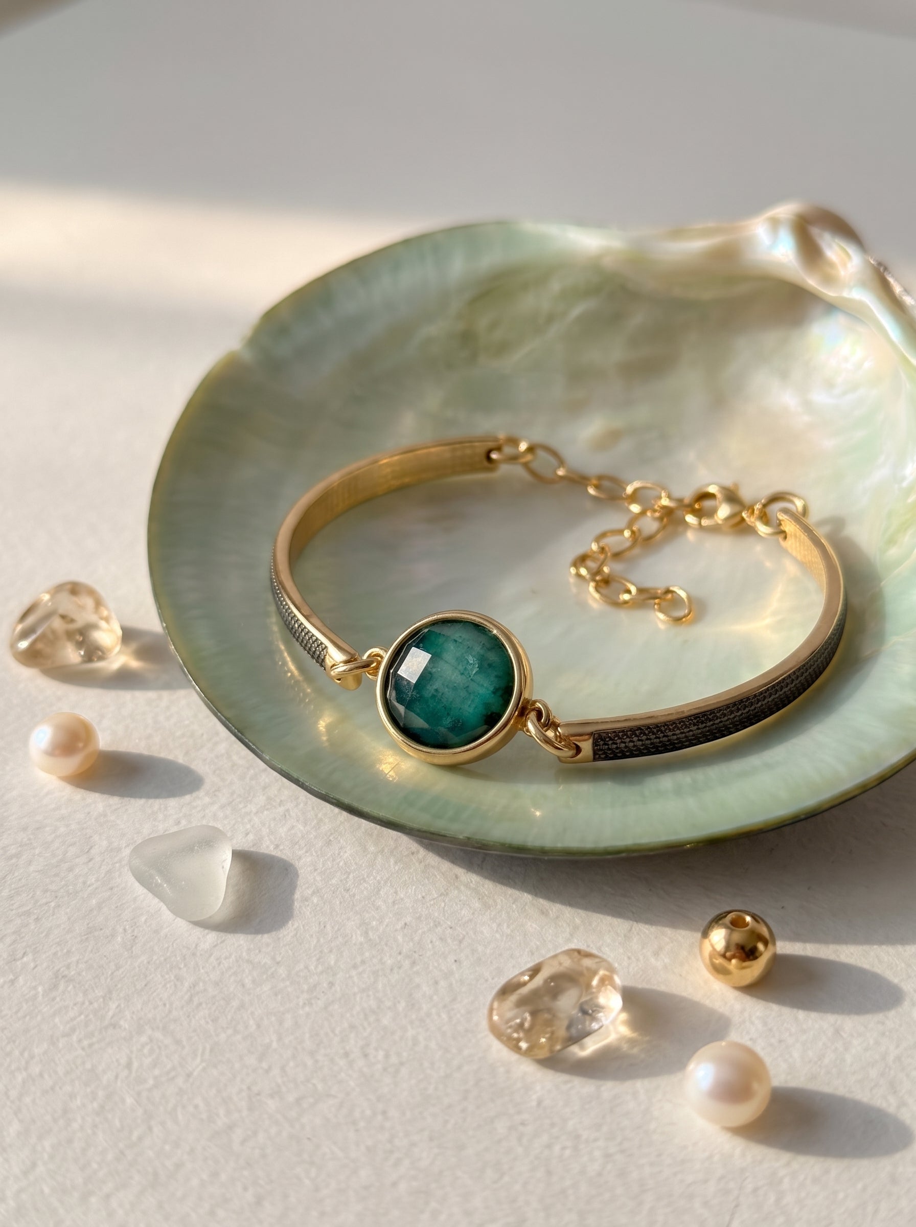 Emerald rock bracelet with gold-plated band and black rhodium plated displayed on a green iridescent shell with crystals and pearls