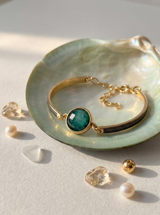 Emerald rock bracelet with gold-plated band and black rhodium plated displayed on a green iridescent shell with crystals and pearls