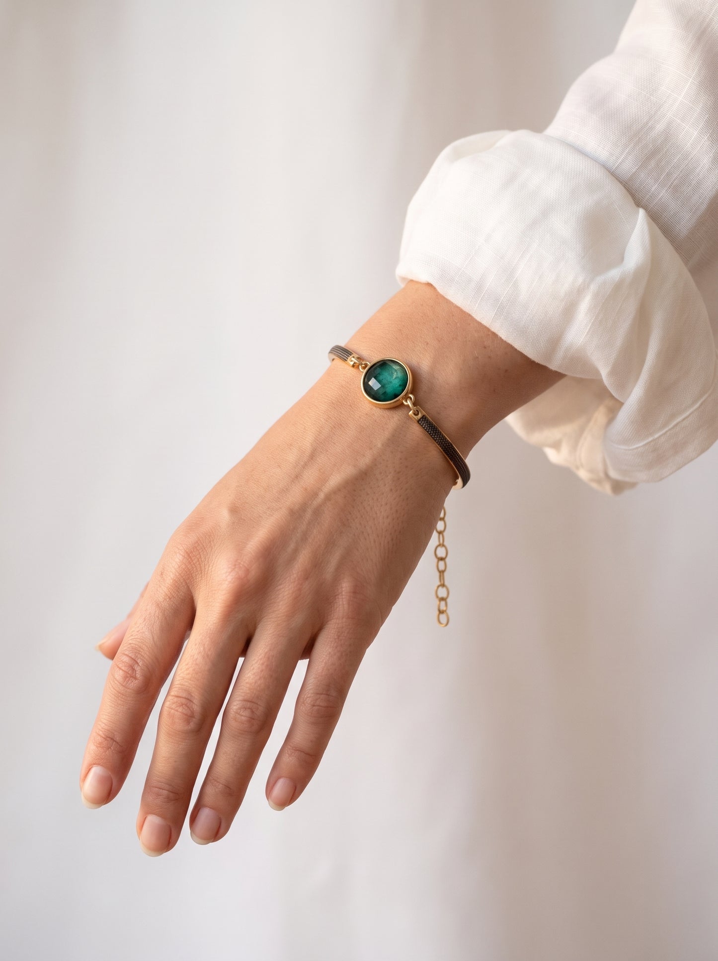 Emerald rock bracelet with gold and black rhodium-plated band worn on a woman's wrist against a white top
