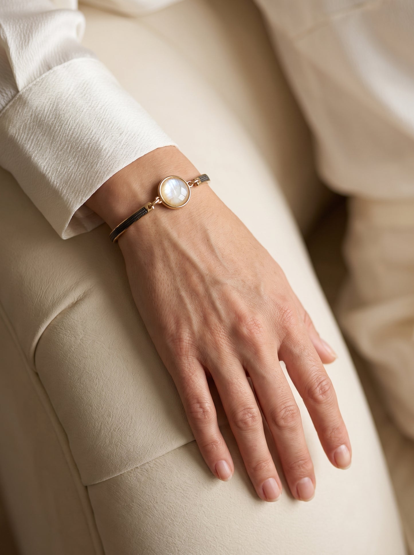 Nautilus shell bracelet with gold and black rhodium-plated band worn on a woman's wrist against a cream blazer