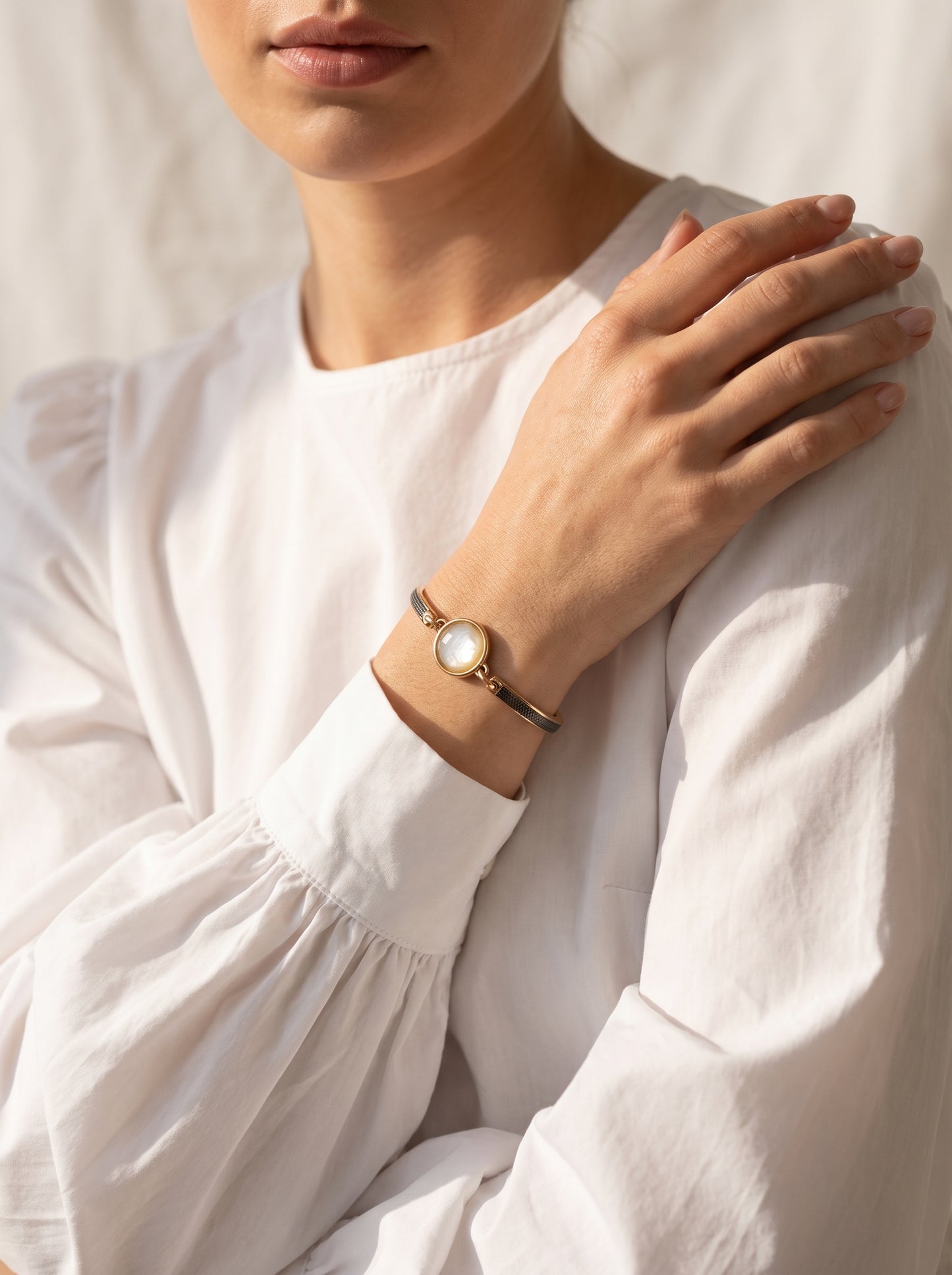 A close-up of a woman wearing a delicate gold-toned  and rhodiu bangle bracelet with a round nautilus shell .