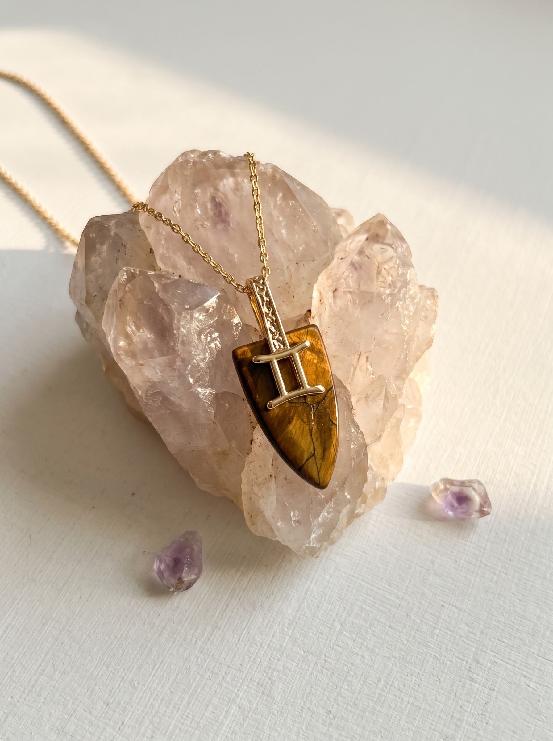 StoneCraft Jewellery tiger's eye Gemini zodiac shield pendant necklace on gold chain, styled on rose quartz crystal with amethyst.