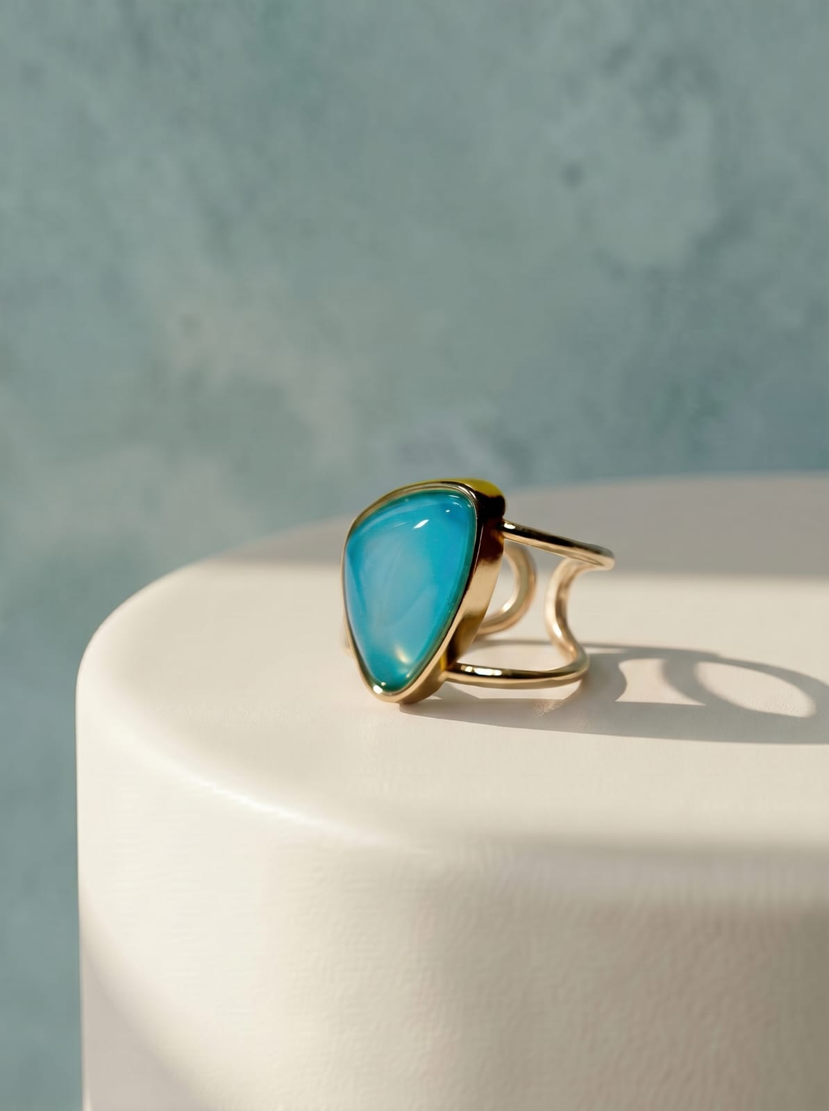 Gold ring with a turquoise stone on a white surface with a light blue background
