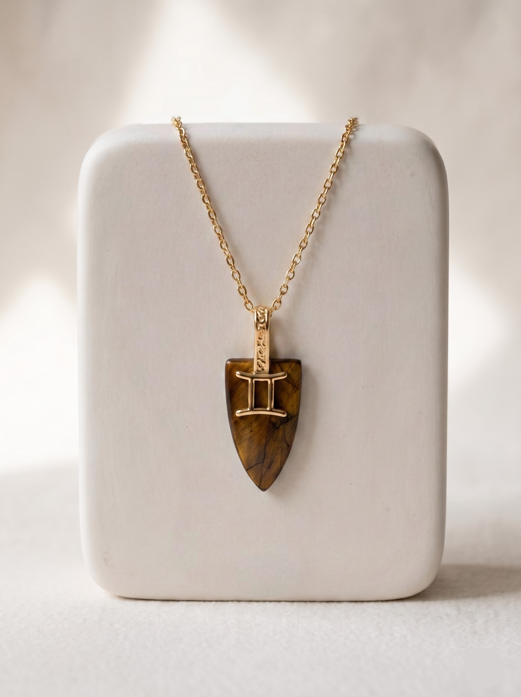 StoneCraft Jewellery tiger's eye Gemini zodiac shield pendant necklace on gold chain, displayed on white ceramic jewellery stand.