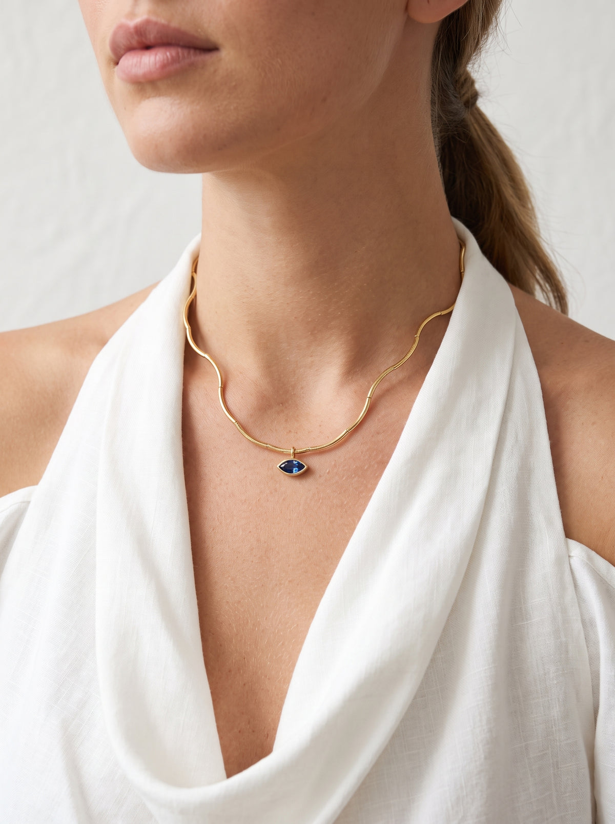 Woman wearing StoneCraft Jewellery Gold Wave Chain Necklace with Blue Crystal Pendant close-up on neck with white halter top
