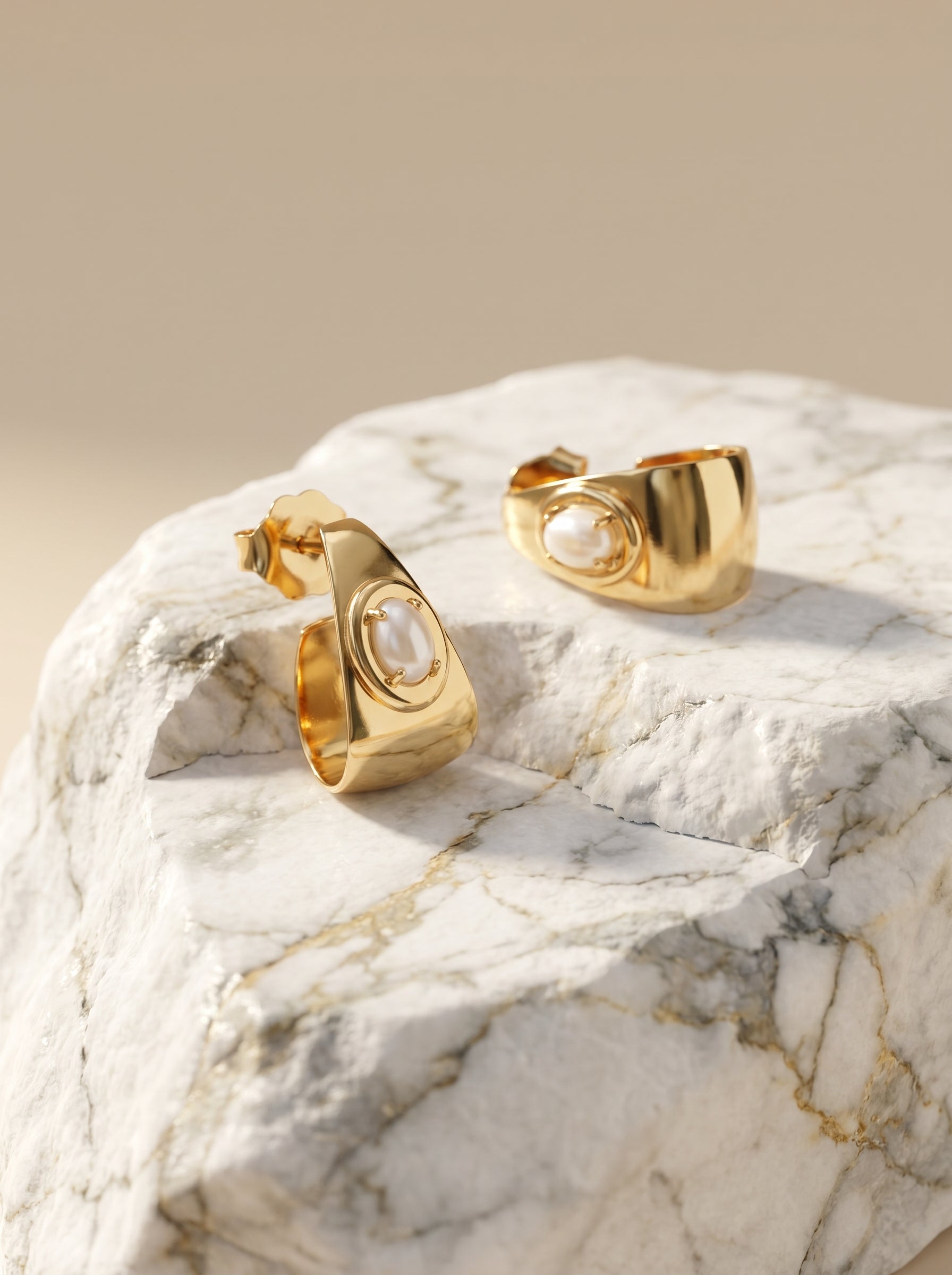Gold-plated half hoop earrings with natural shell cabochon displayed on marble stone