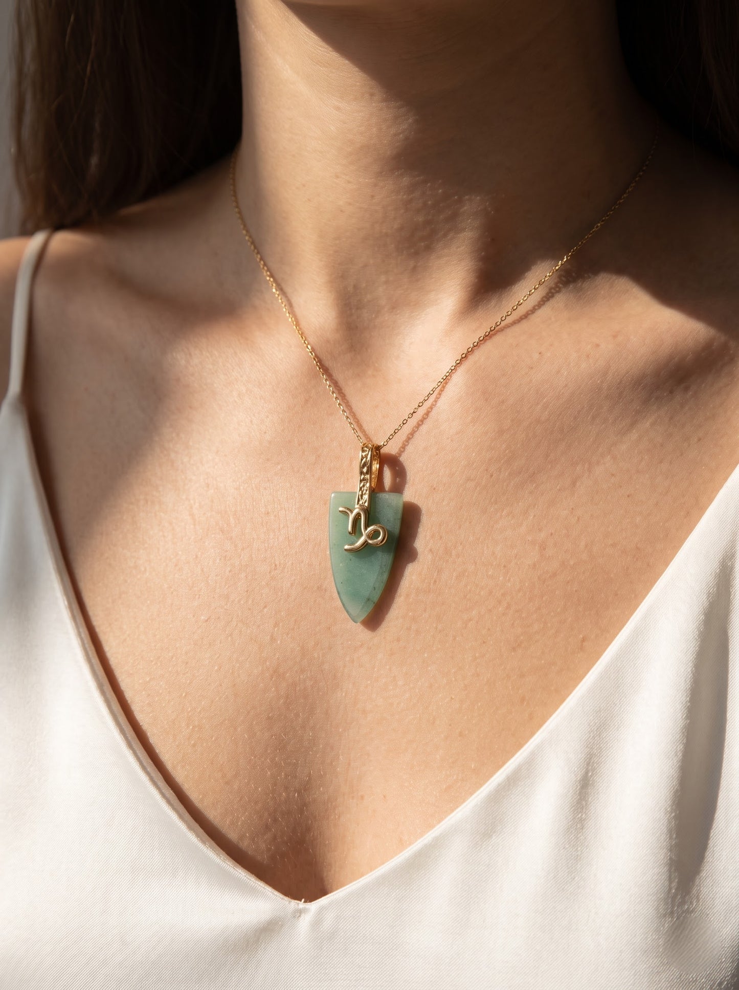 Woman wearing StoneCraft Jewellery green aventurine Virgo zodiac arrowhead pendant necklace on gold chain, V-neck white linen top.