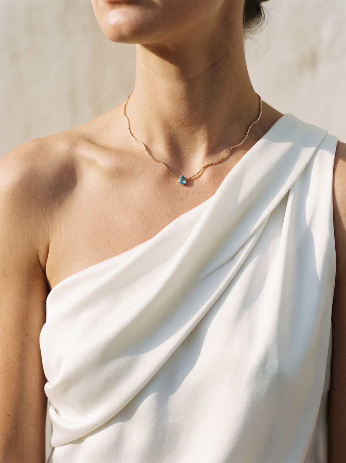 StoneCraft Jewellery gold wave chain necklace with a light blue teardrop crystal pendant draped over a pale crystal cluster.