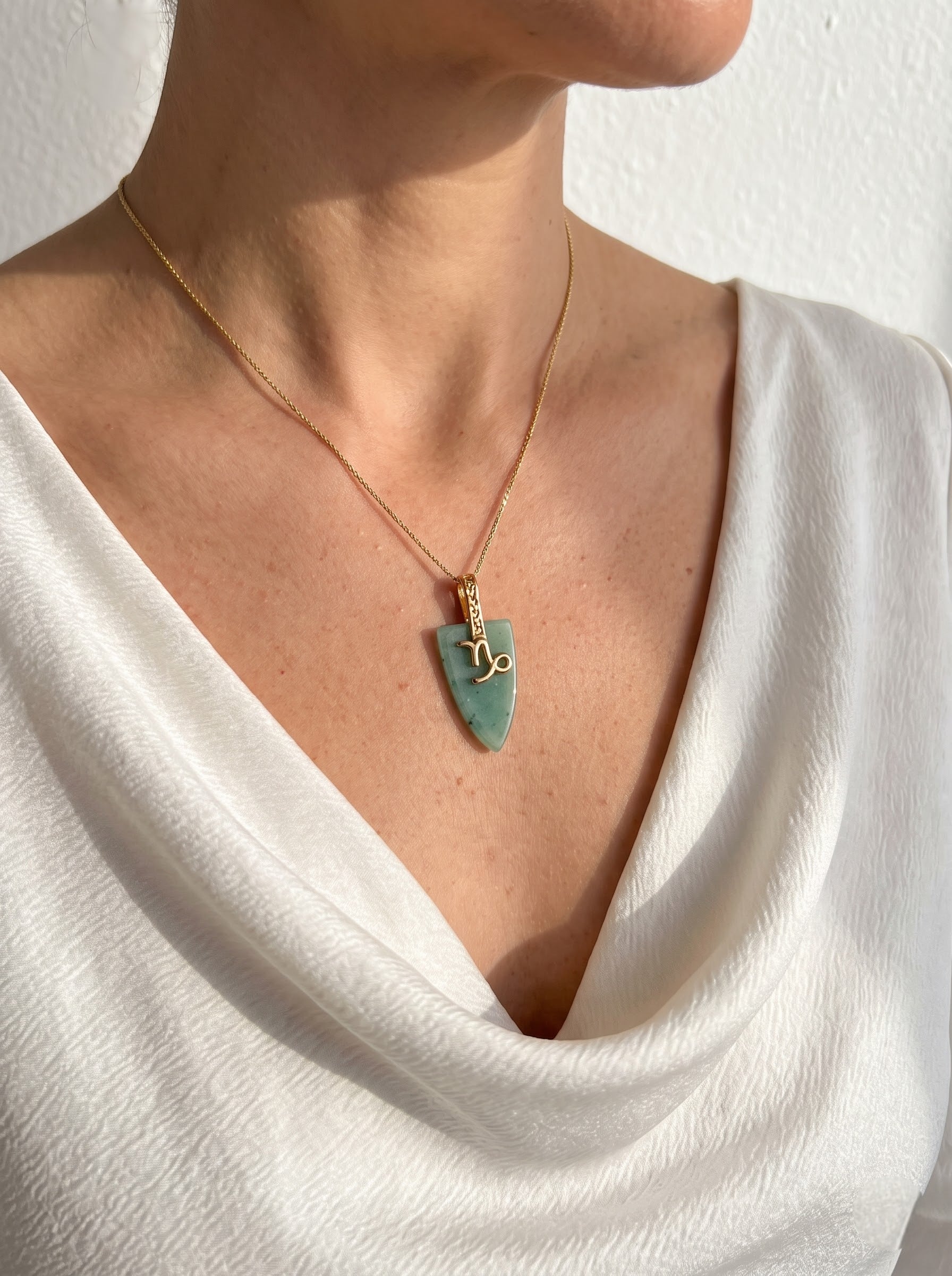 Woman wearing StoneCraft Jewellery green aventurine Virgo zodiac arrowhead pendant necklace on gold chain, draped white top editorial shot.