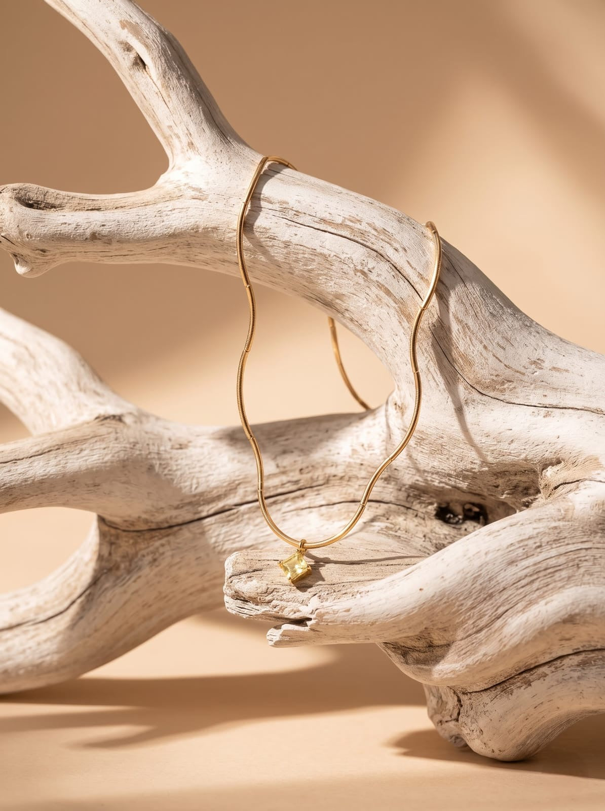 StoneCraft Jewellery gold wave chain necklace with a pale yellow square crystal pendant draped over pale driftwood.