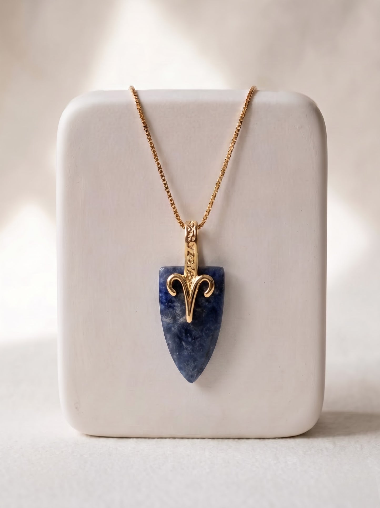 StoneCraft Jewellery sodalite Aries zodiac arrowhead pendant necklace on gold box chain, displayed on white ceramic jewellery stand.