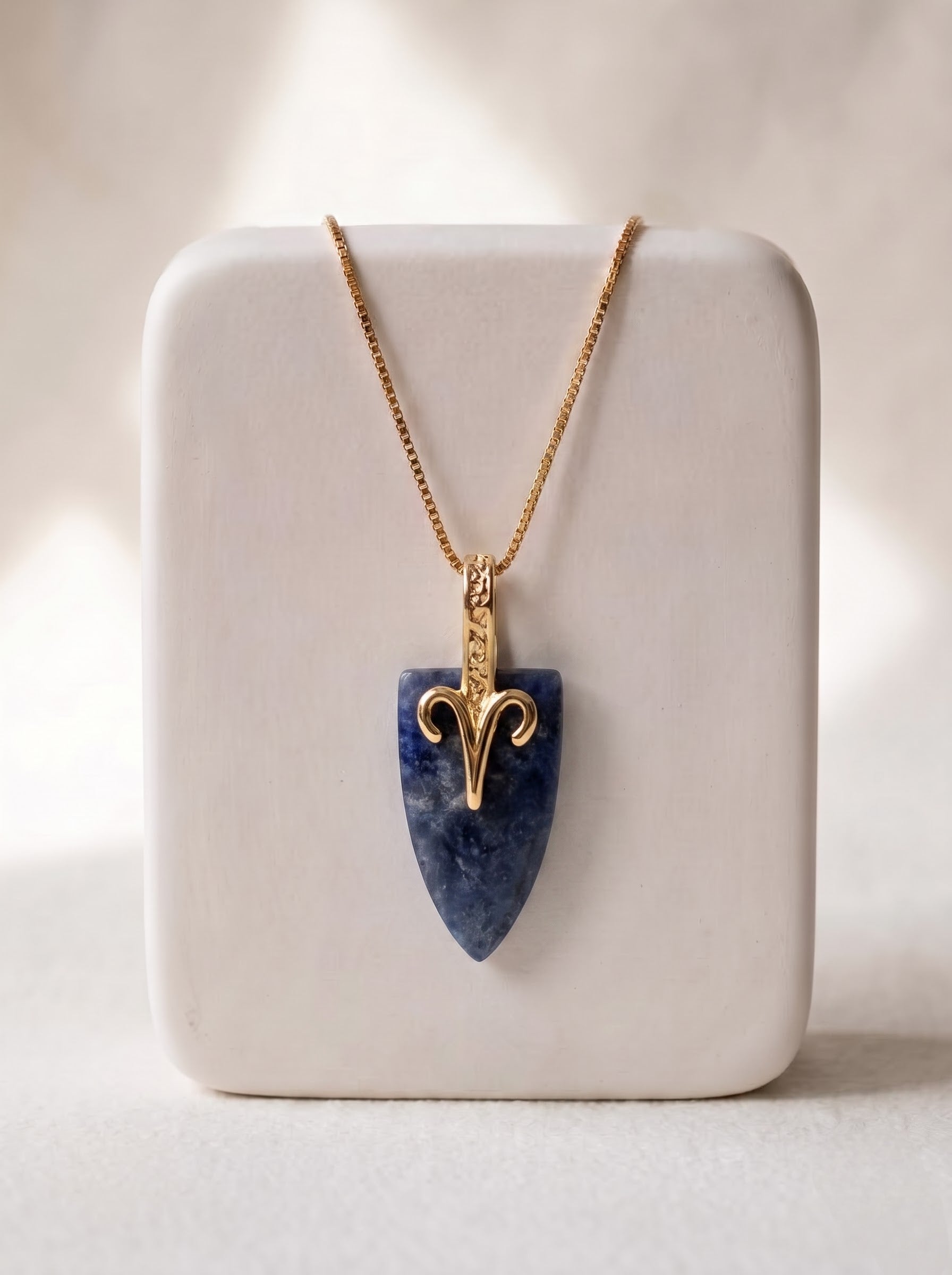 StoneCraft Jewellery sodalite Aries zodiac arrowhead pendant necklace on gold box chain, displayed on white ceramic jewellery stand.