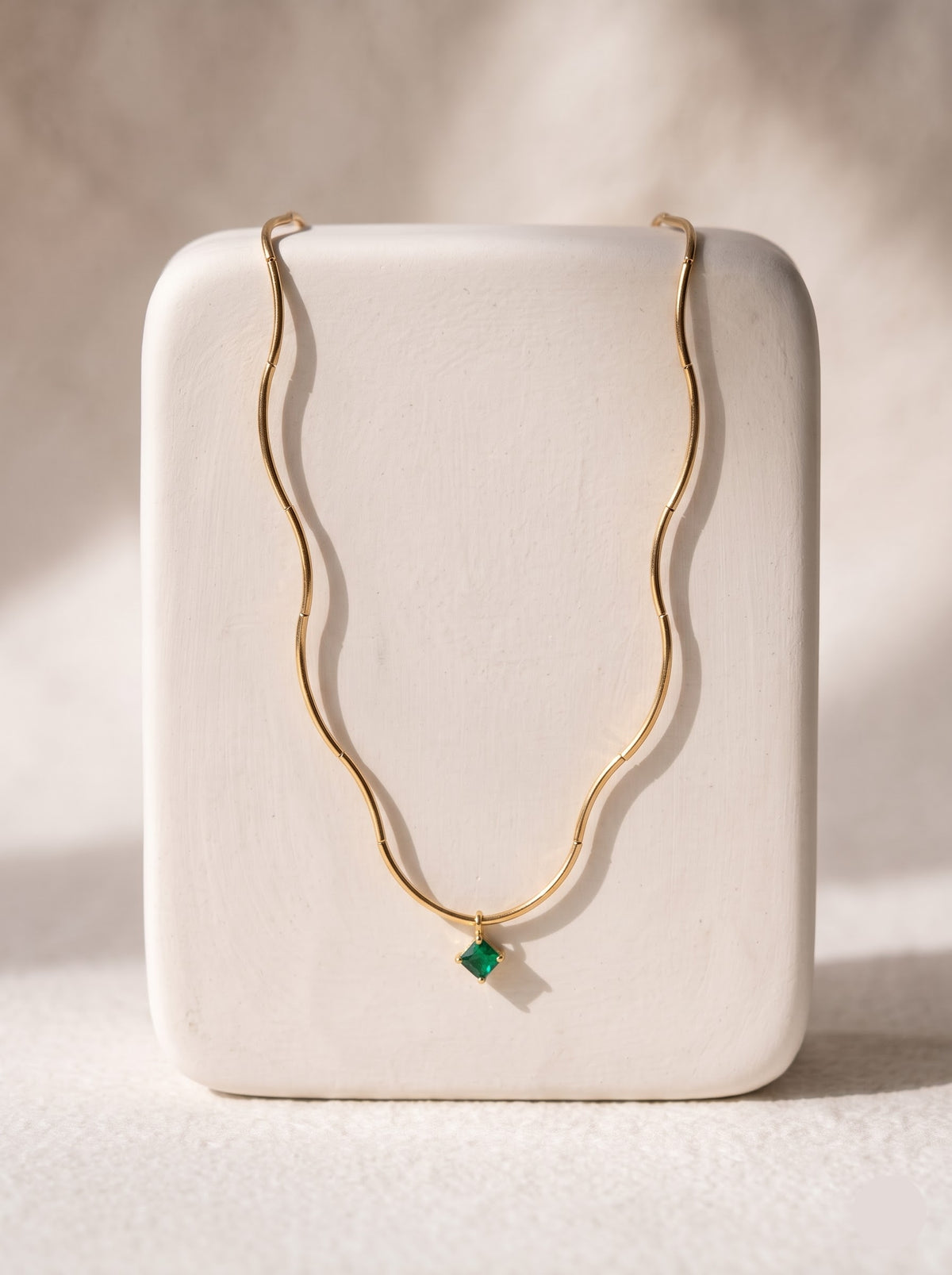 StoneCraft Jewellery gold wave chain necklace with a square green crystal pendant draped beneath a green glass dish.
