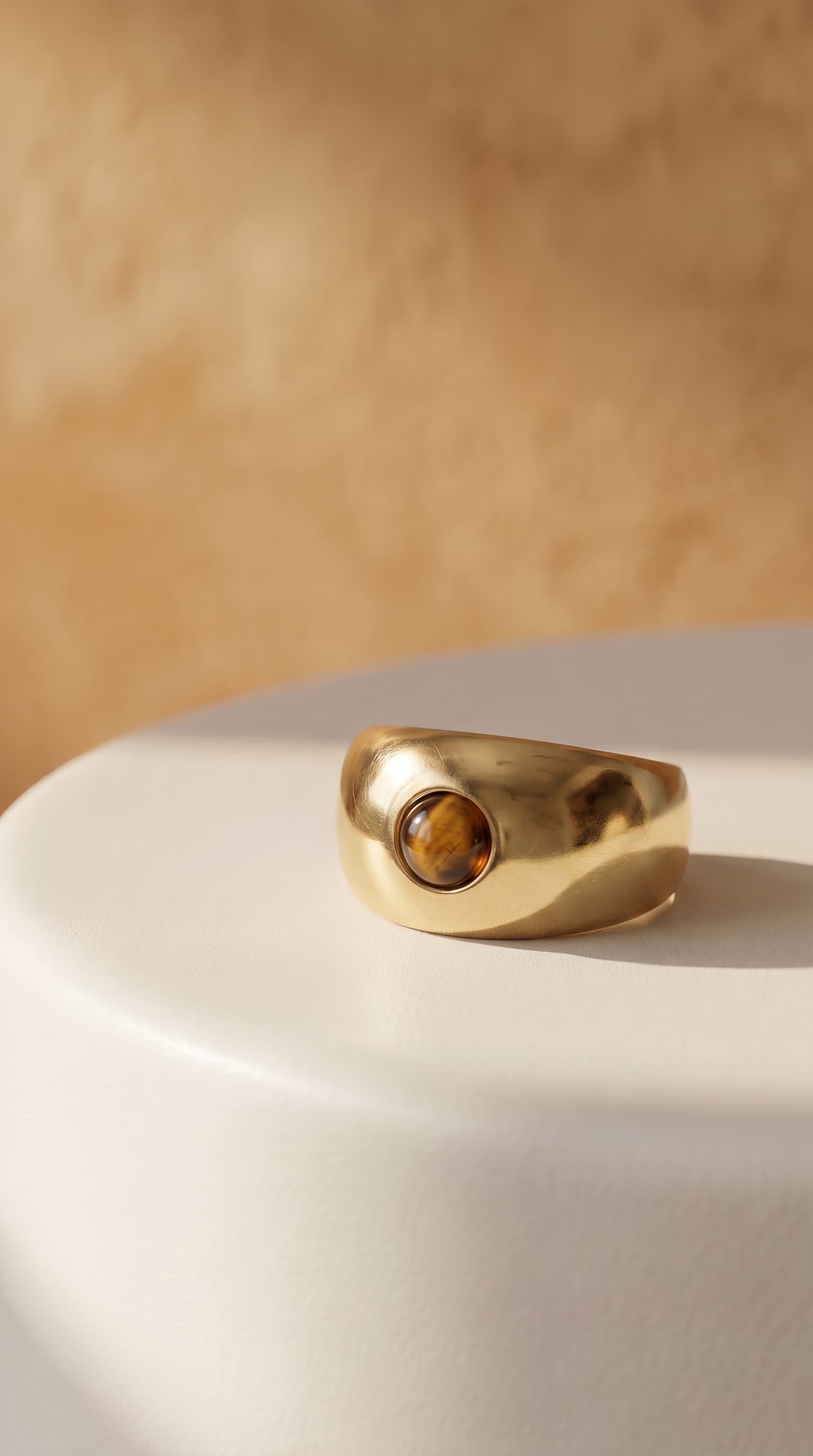 Close-up of model wearing gold multi-stone ring with mother of pearl and rose quartz stones, hand raised near face