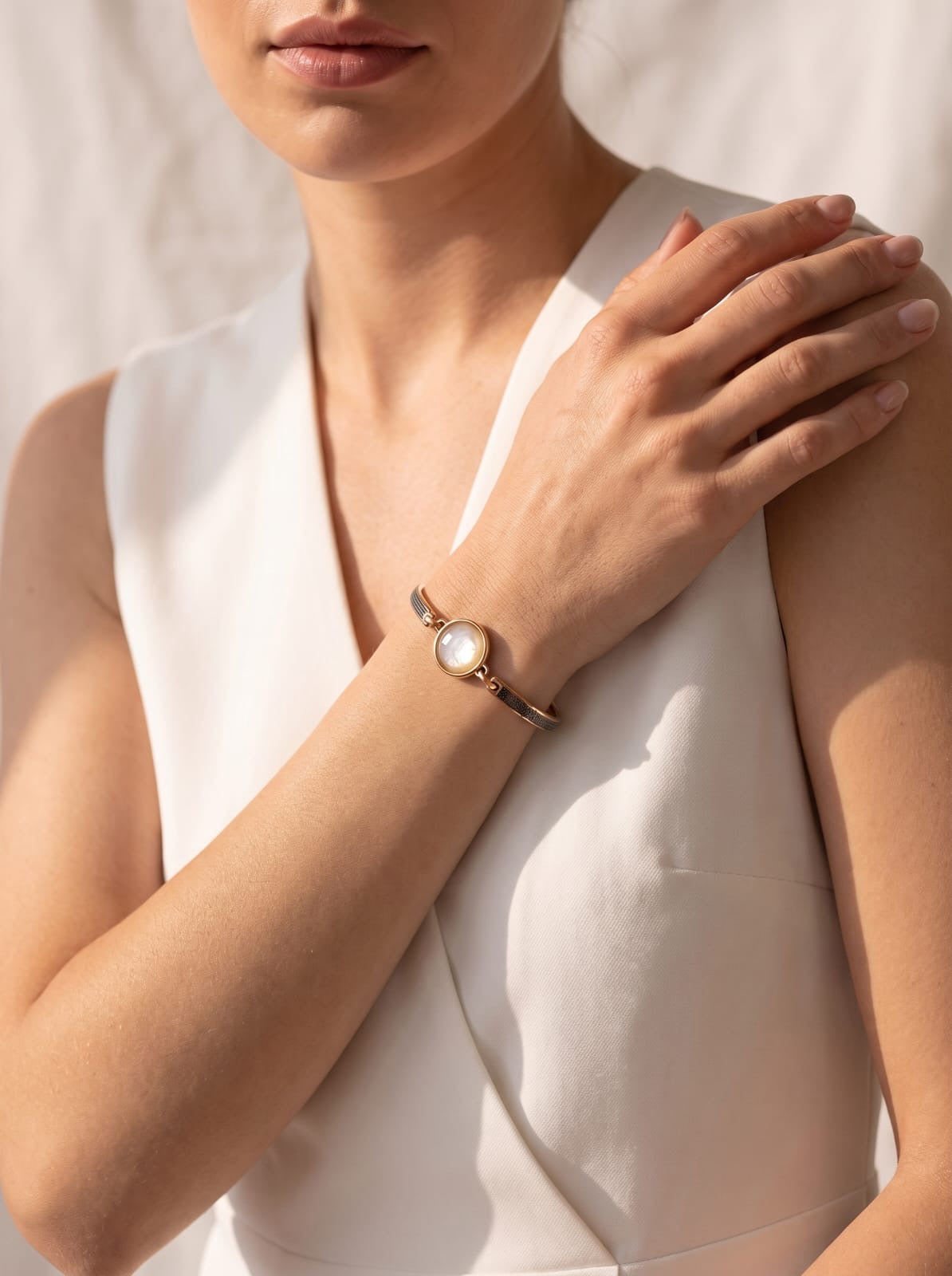 a slim gold and black rhodium plated cuff bracelet with a nautilus shell centerpiece, styled with a white sleeveless top under warm natural light.