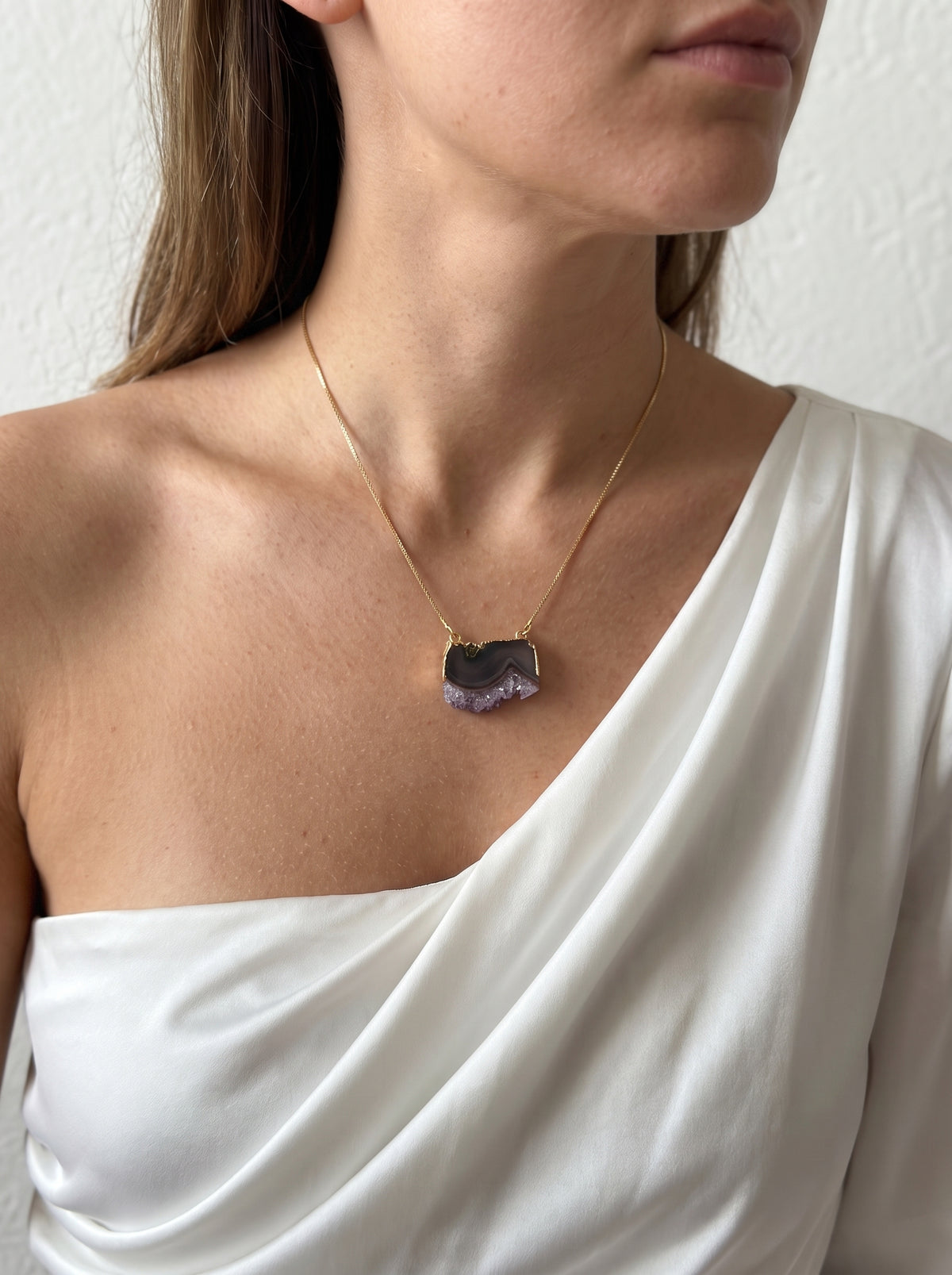 Model wearing a StoneCraft Jewellery purple crystal slice pendant necklace with a white one-shoulder top, close-up.