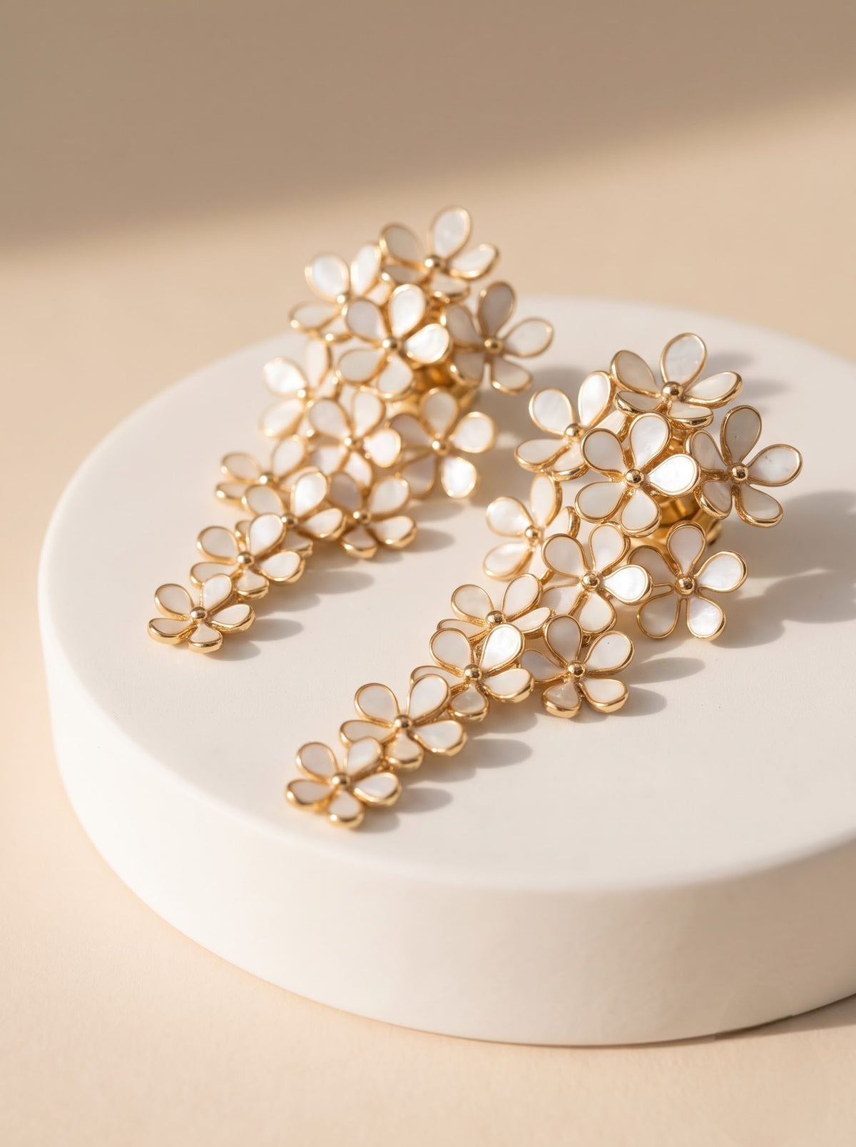 Pair of StoneCraft Jewellery white floral cascade earrings with gold-plated outlines displayed on a textured stone surface.