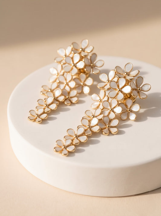 Pair of StoneCraft Jewellery white floral cascade earrings with gold-plated outlines displayed on a textured stone surface.