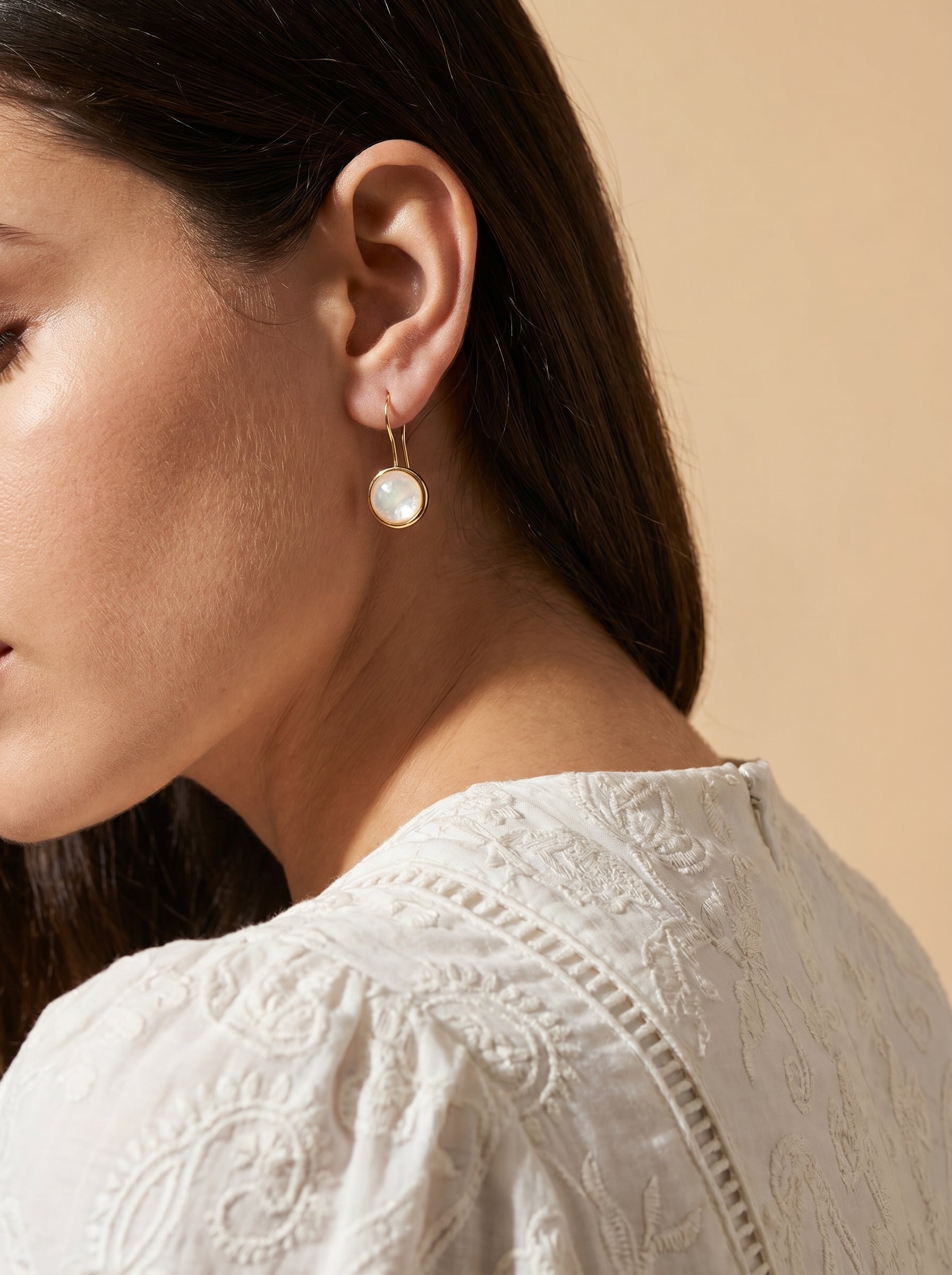 Close-up of a woman wearing a gold earring with a beige background