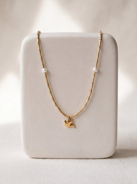 Gold-plated beaded necklace with two freshwater pearls and a gold flying bird charm pendant displayed on a white jewellery stand