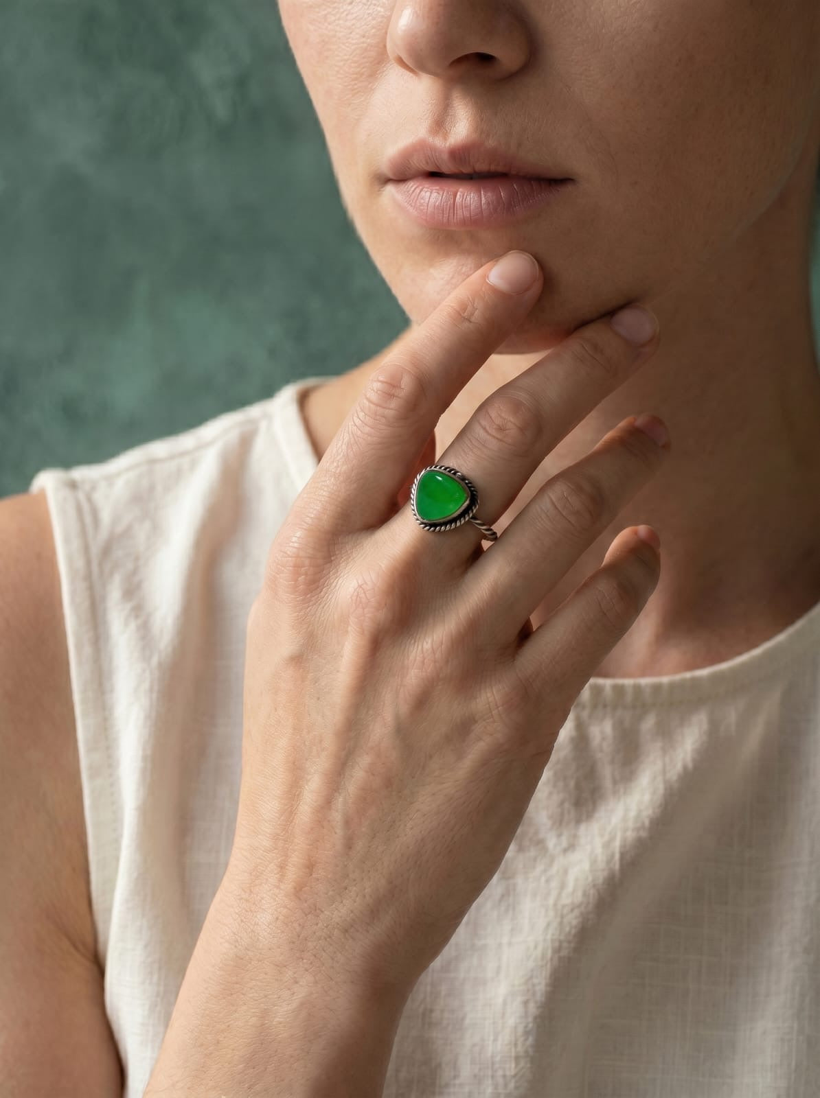 Close-up of a person wearing a green jade kite shape ring on a neutral background