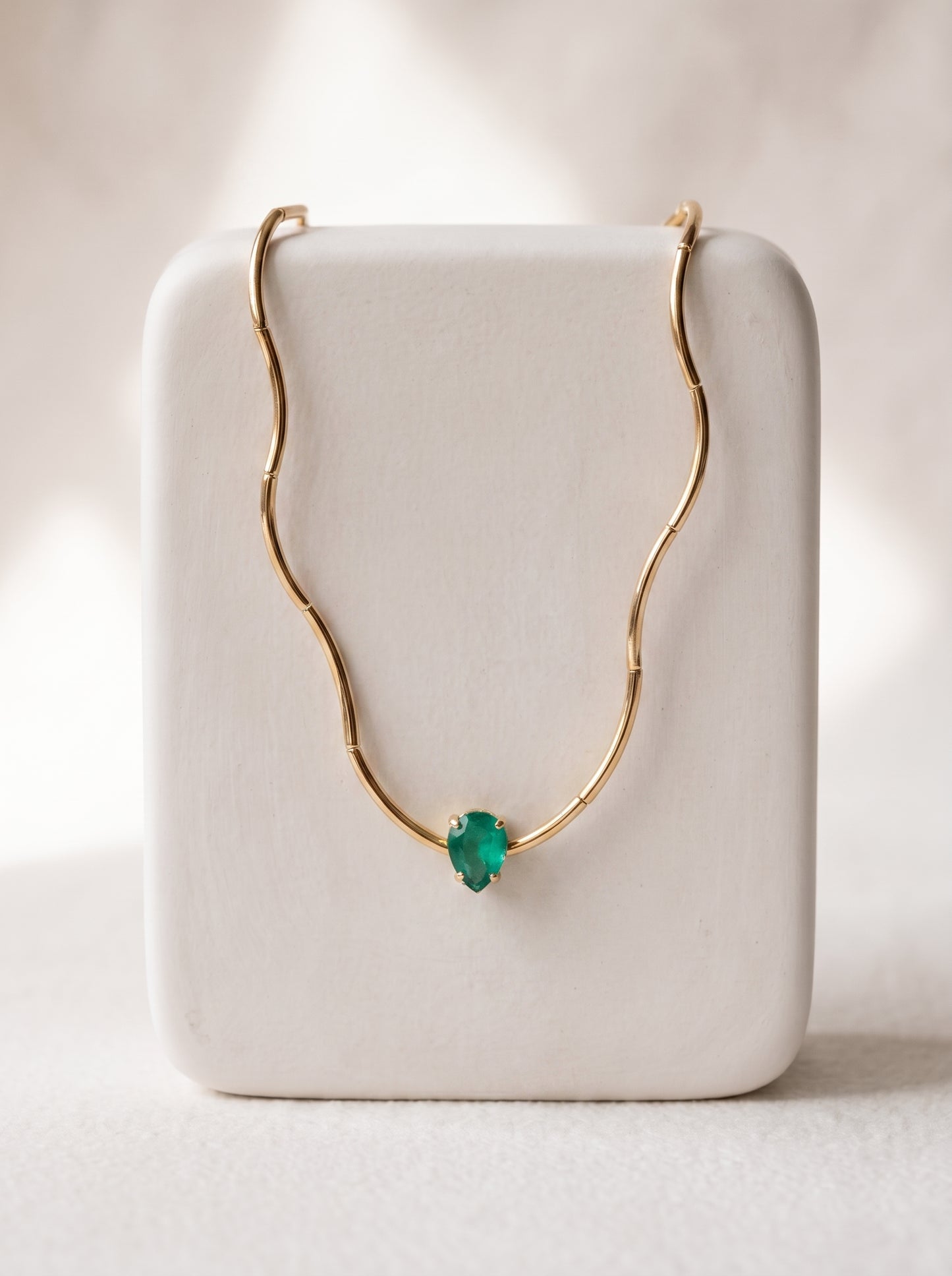Gold-plated bamboo bar chain necklace with pear-cut green crystal solitaire displayed on a white jewellery stand