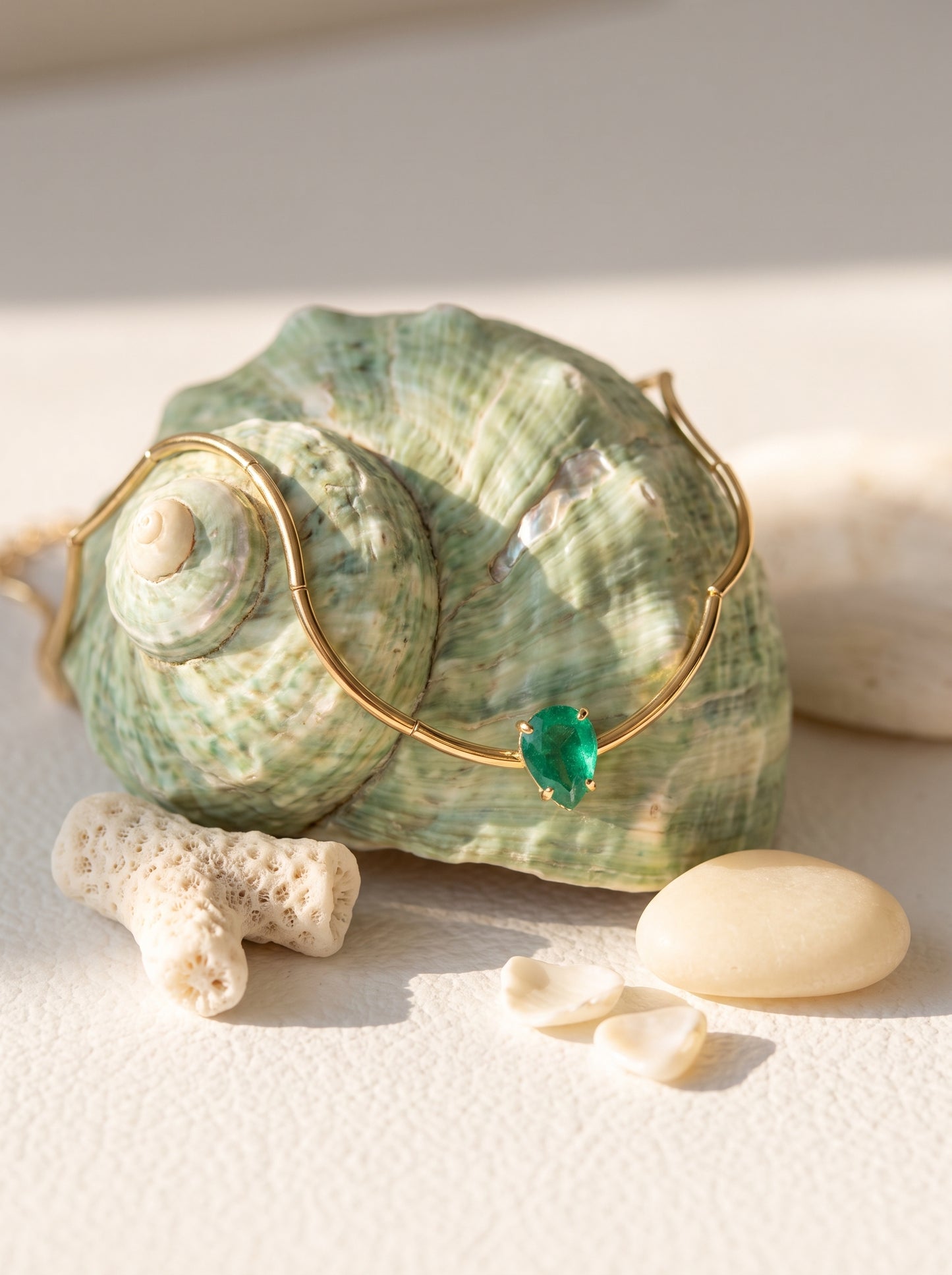  Green crystal solitaire bamboo chain necklace draped over a large green shell surrounded by coral and pebbles